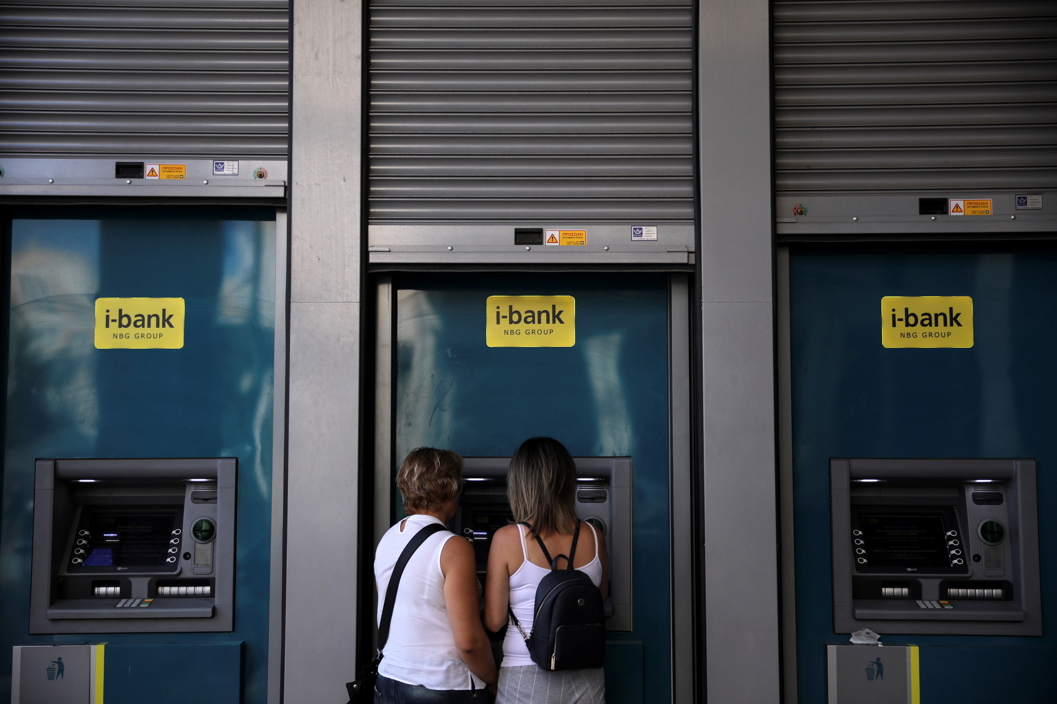 Two women use an ATM outside a National Bank branch in Athens