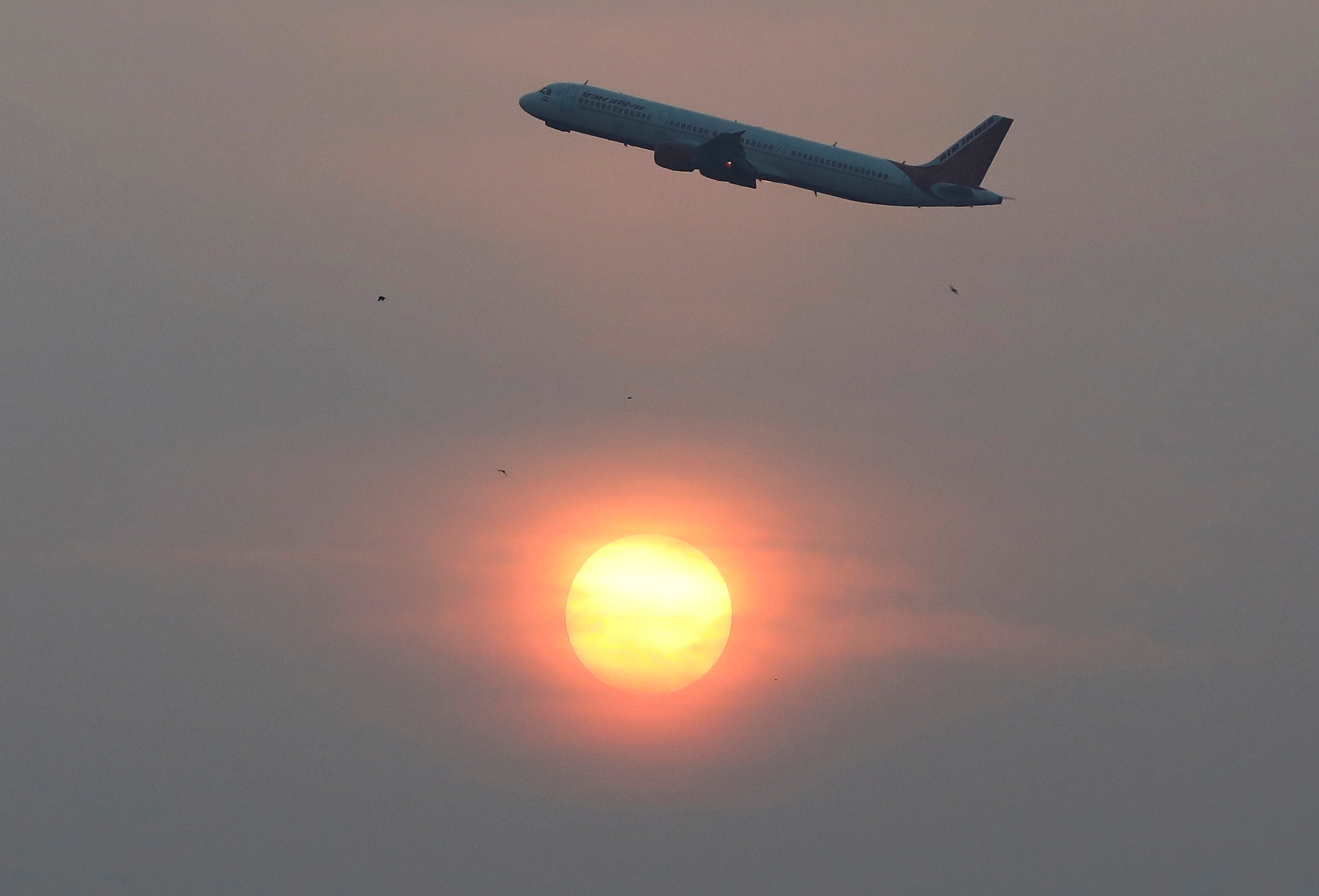 An Air India passenger plane passes the sun on a smoggy morning in Ahmedabad