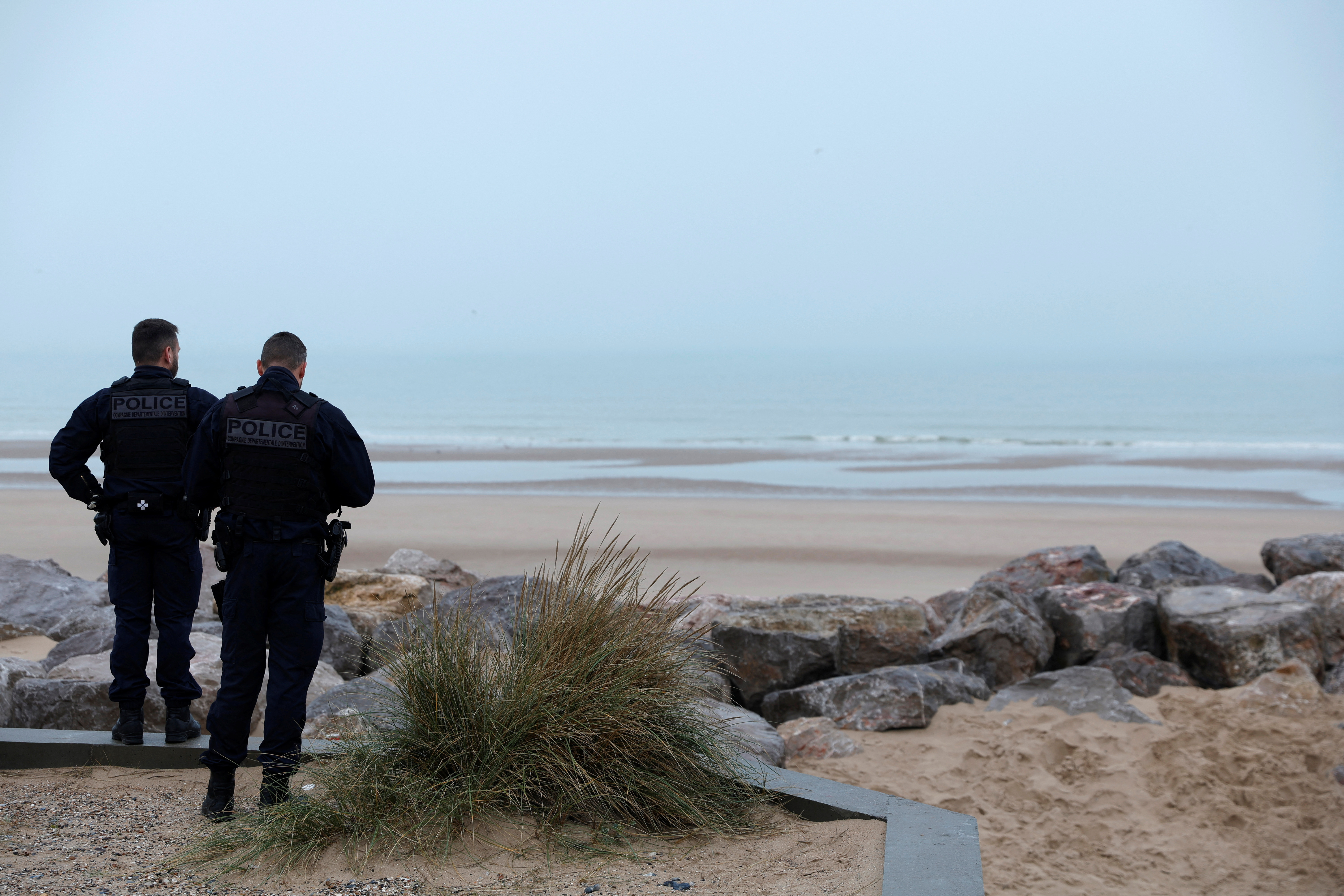 French police look at the coastline from a beach in Sangatte near Calais