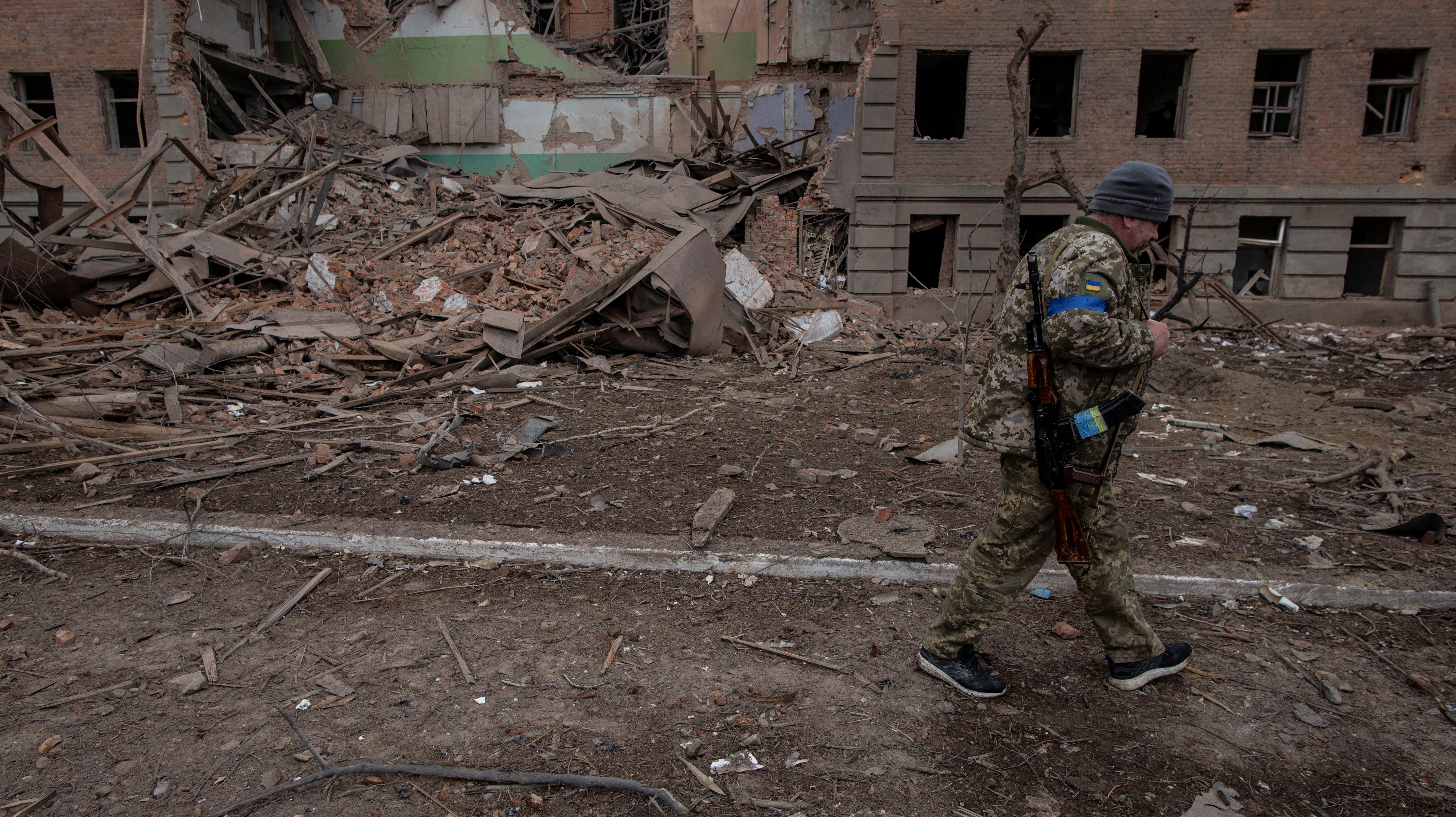 A Ukrainian service member walks past a destroyed building in the town of Okhtyrka