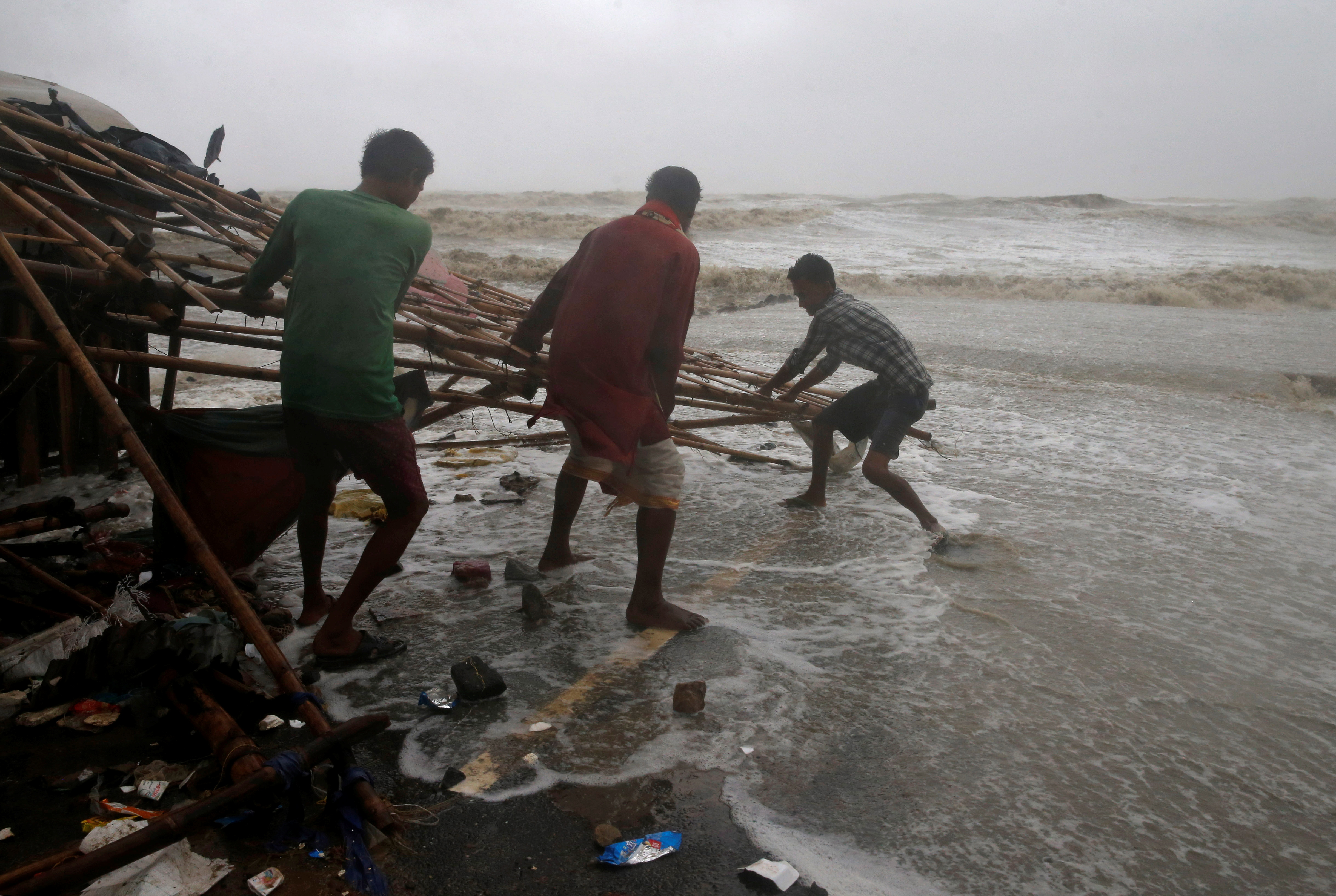 Men remove bamboo rooftop of a stall damaged by heavy winds at a shore ahead of Cyclone Yaas in Bichitrapur