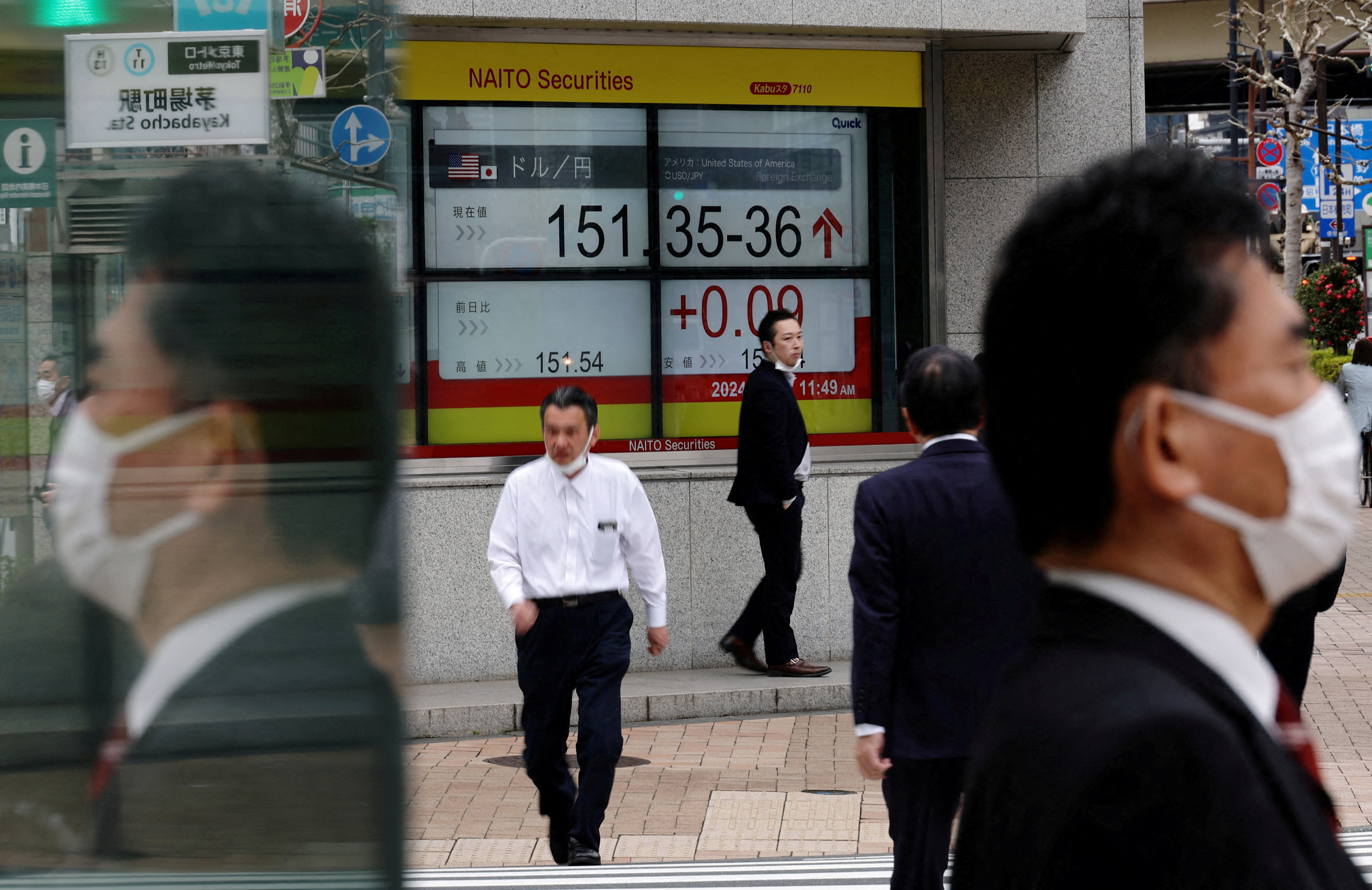 Pedestrians walk past an electric monitor displaying the Japanese yen exchange rate against the U.S. dollar outside a brokerage in Tokyo