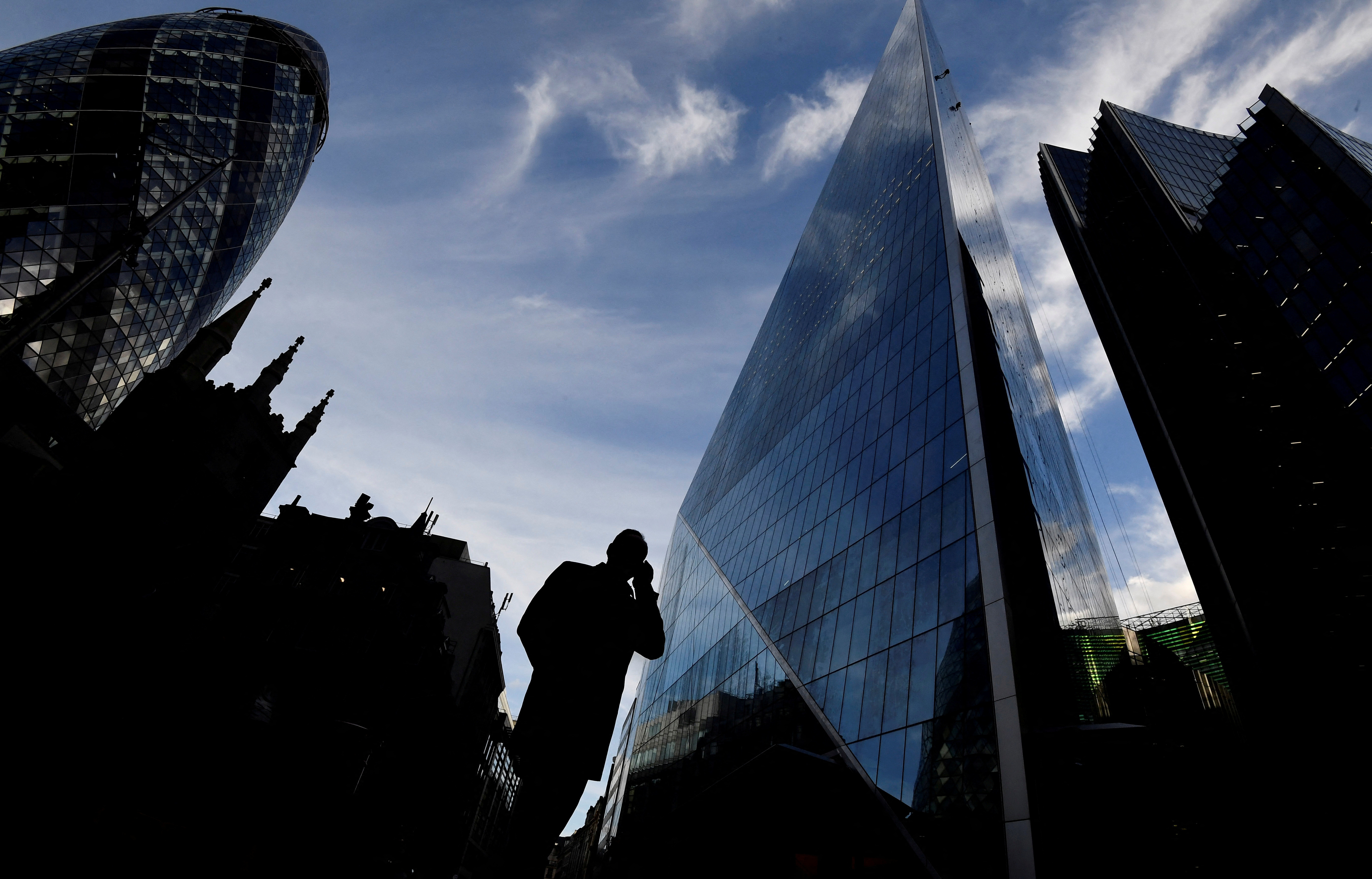 A man speaks on his phone as he walks past the Gherkin and other office buildings in the City of London