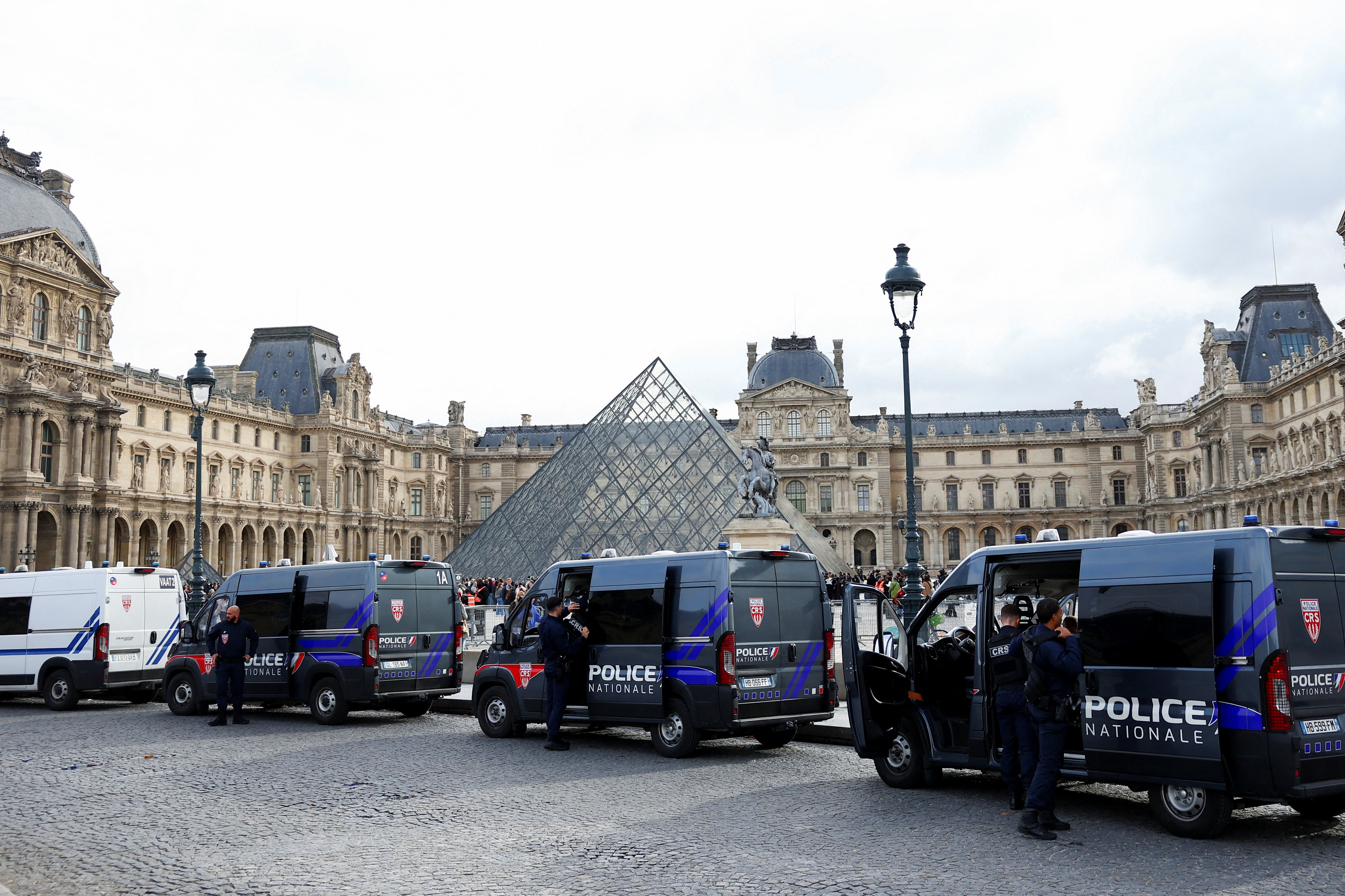 French police vans are parked near the glass Pyramid of the Louvre Museum