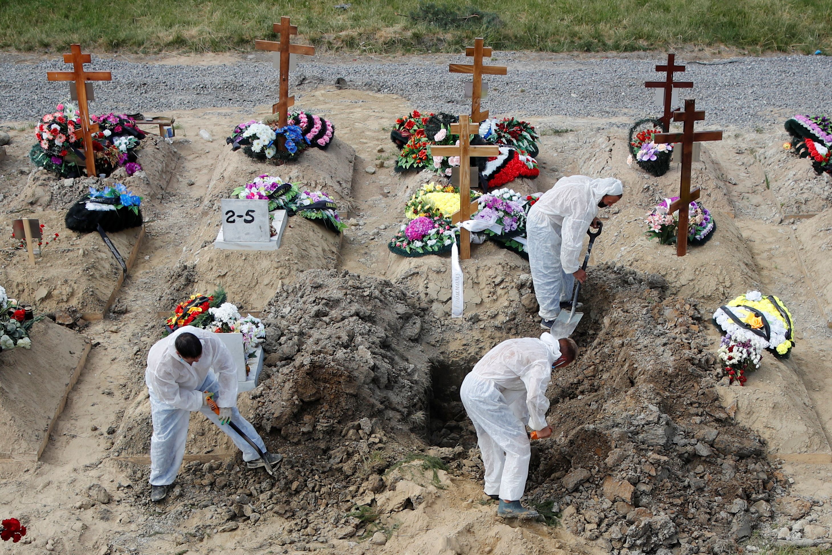 Grave diggers wearing personal protective equipment bury a person at a graveyard in Saint Petersburg