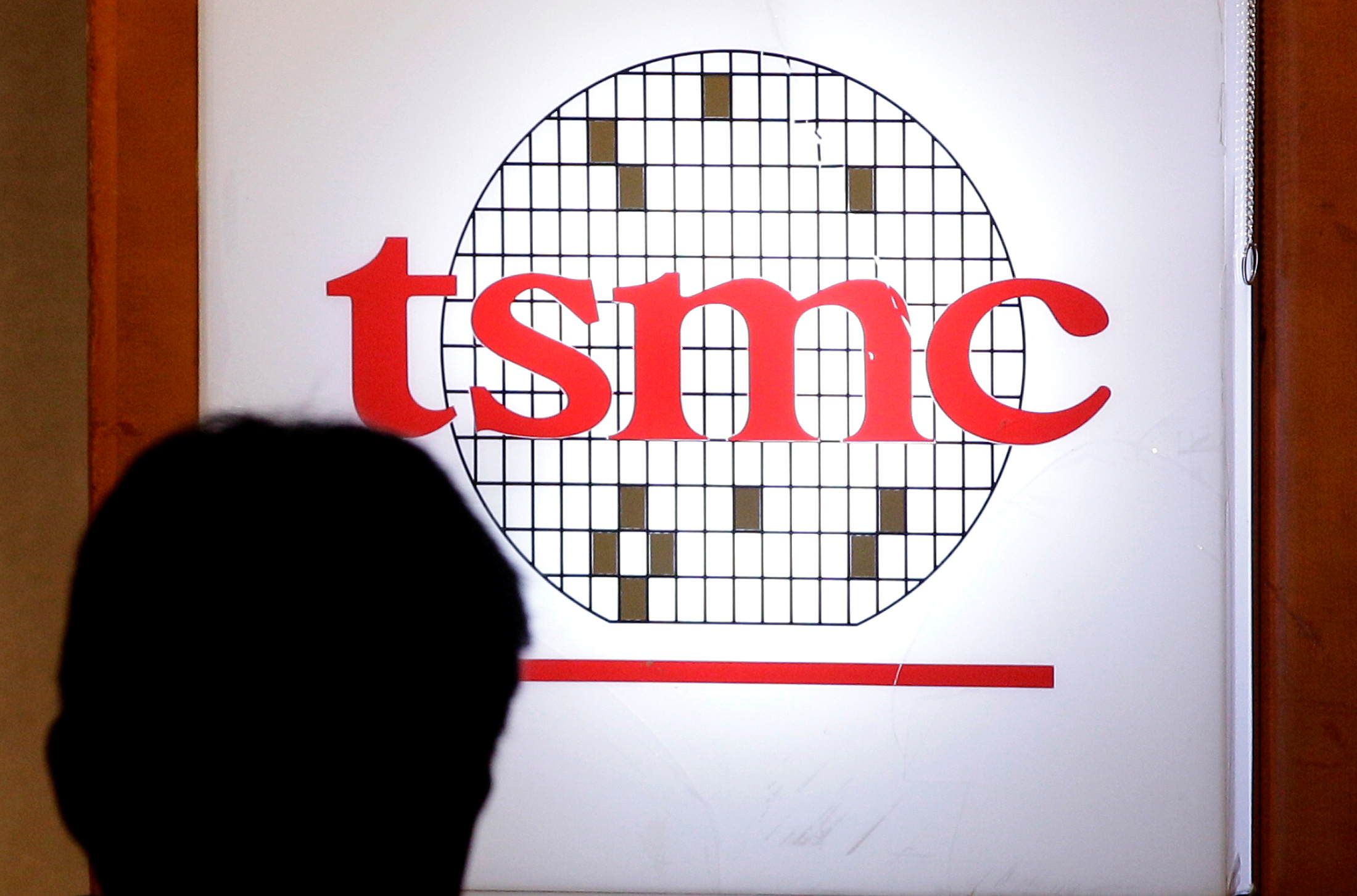 A man sits in front of the logo of Taiwan Semiconductor Manufacturing Co Ltd (TSMC) during an investors' conference in Taipei
