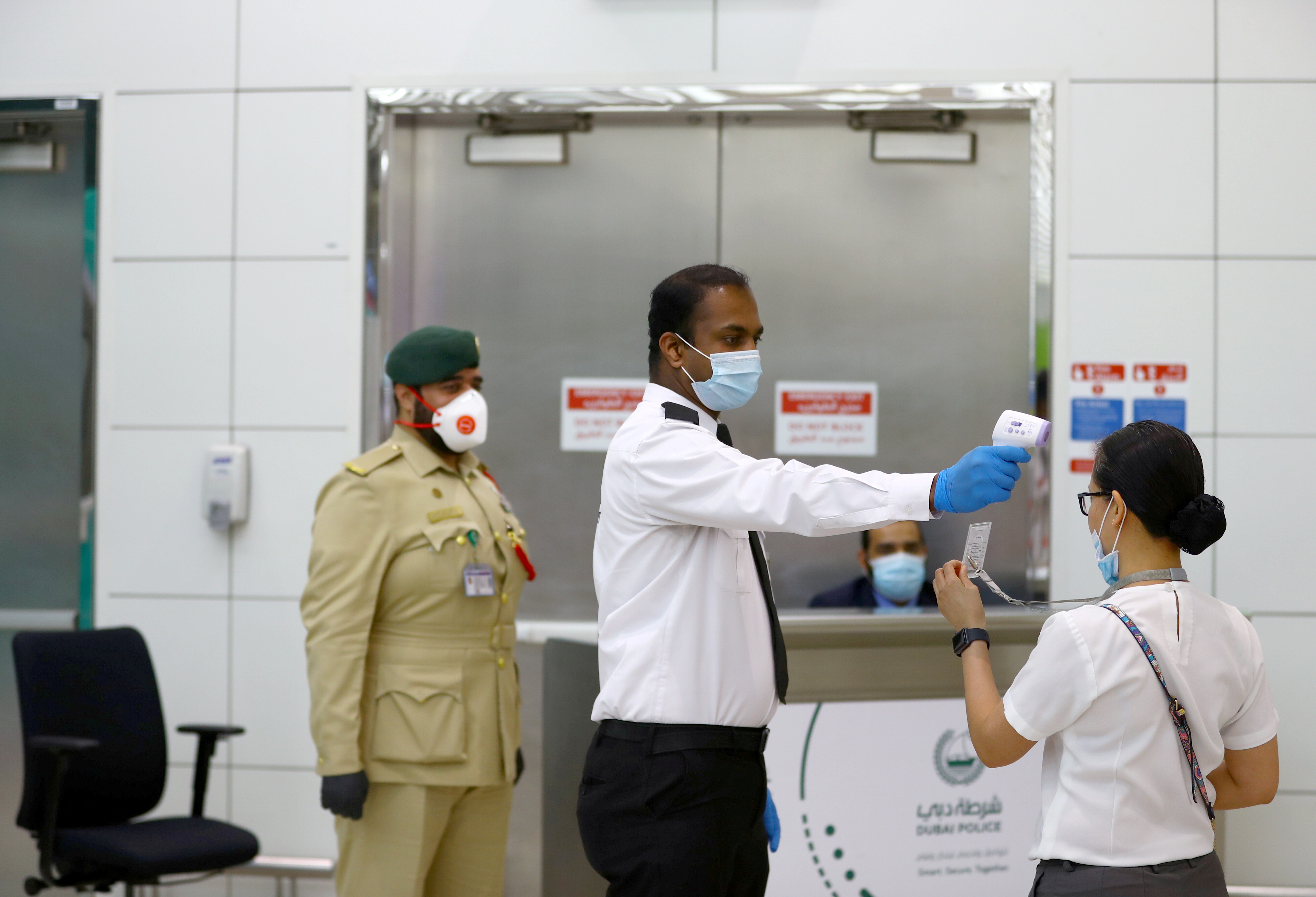 A security man takes temperature of a woman amid the outbreak of the coronavirus disease (COVID-19) at Dubai International Airport