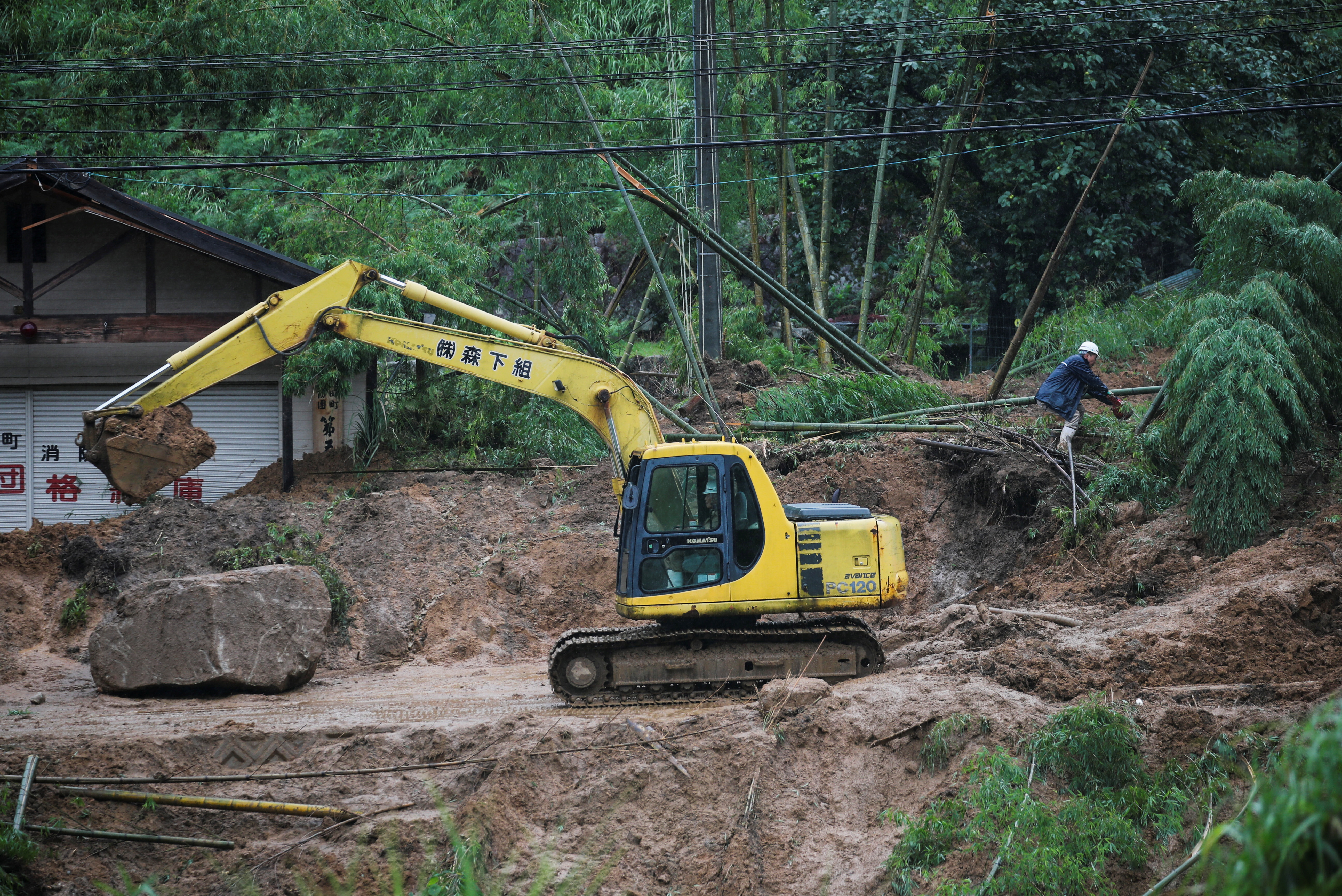 Workers clear a site where a landslide left a 75-year-old woman injured after heavy rain in Soeda