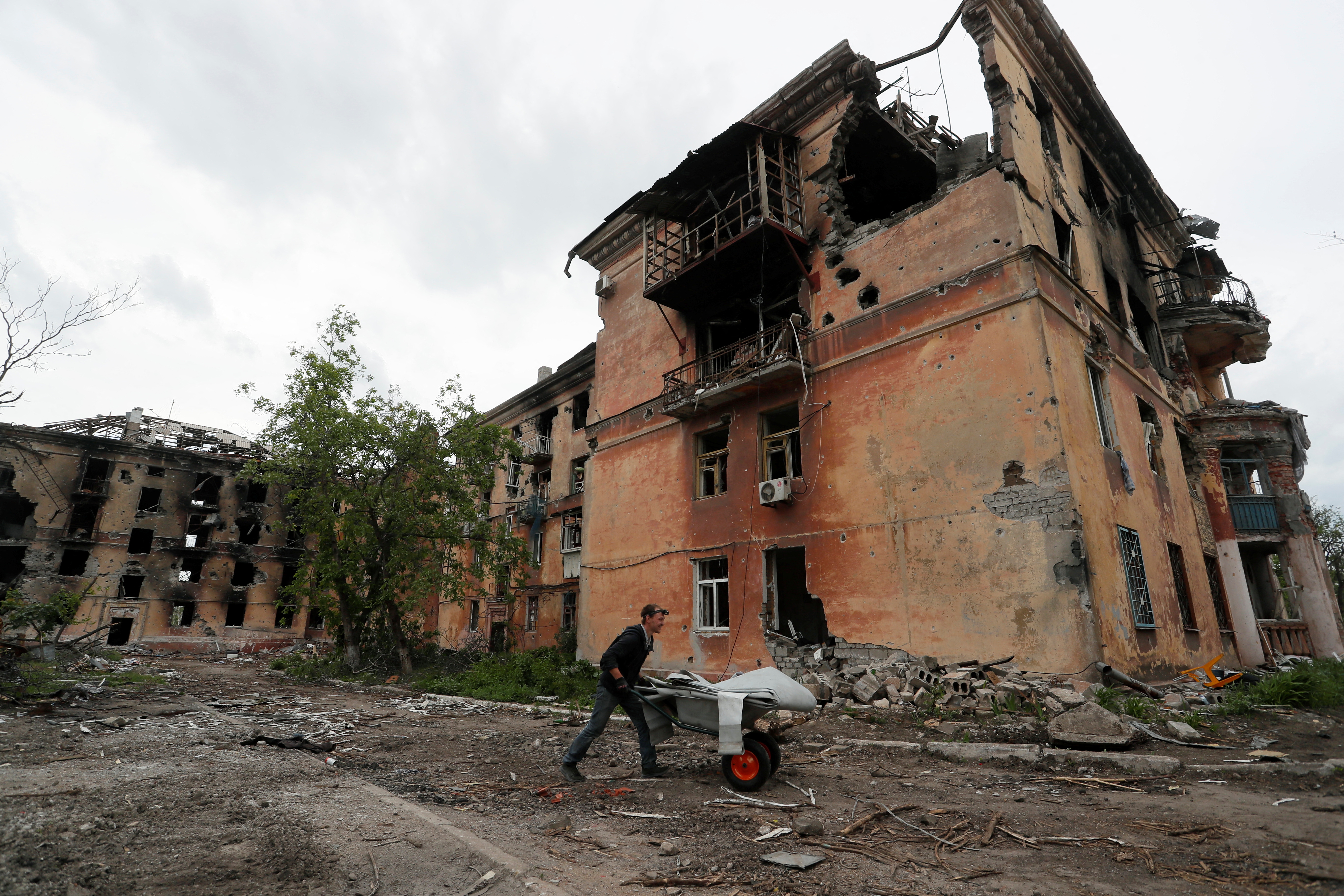 A local resident pushes a wheelbarrow past a heavily damaged apartment building in Mariupol