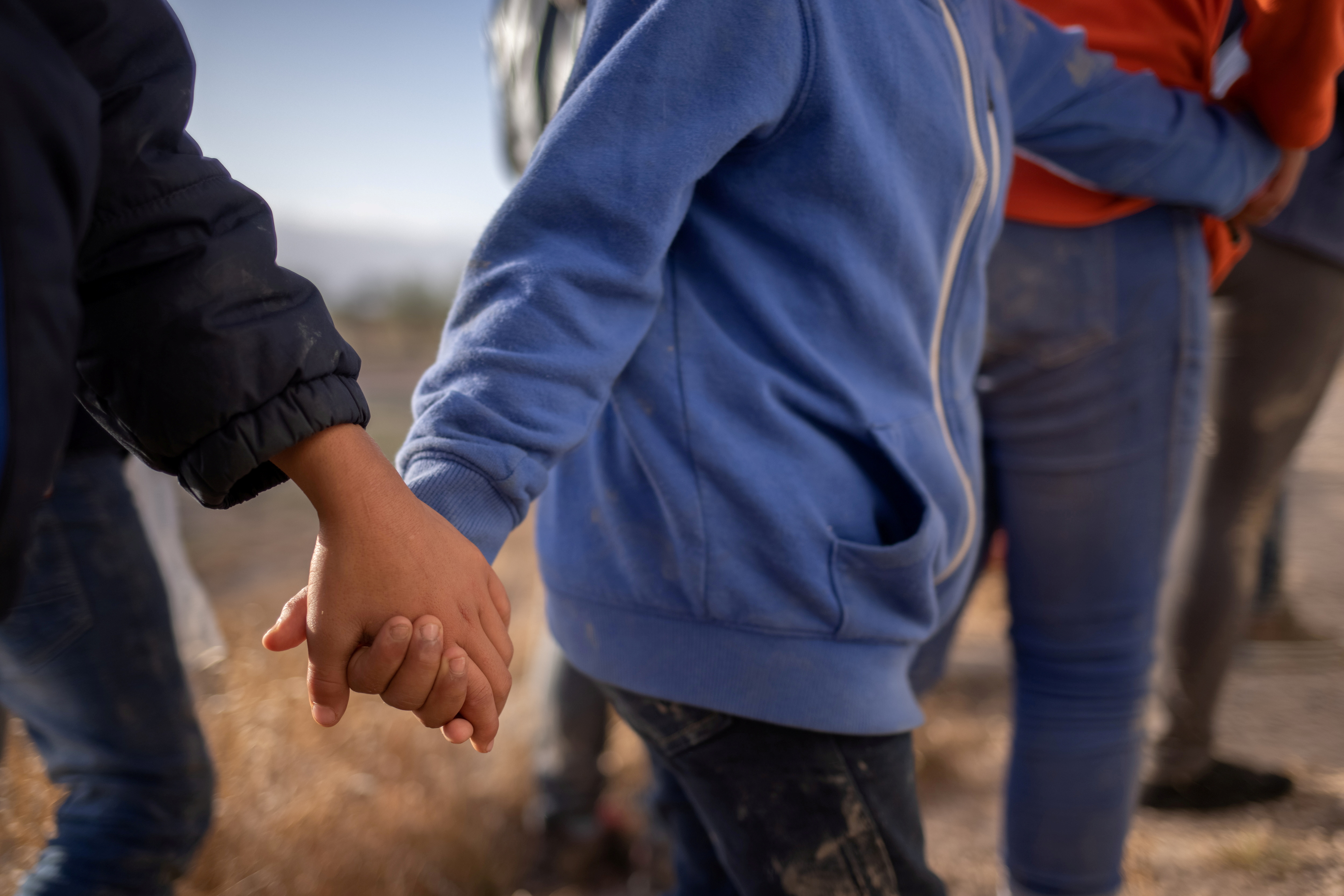 Asylum seeking unaccompanied minors hold hands amid adult migrants from Central America as they await transport in Penitas, Texas