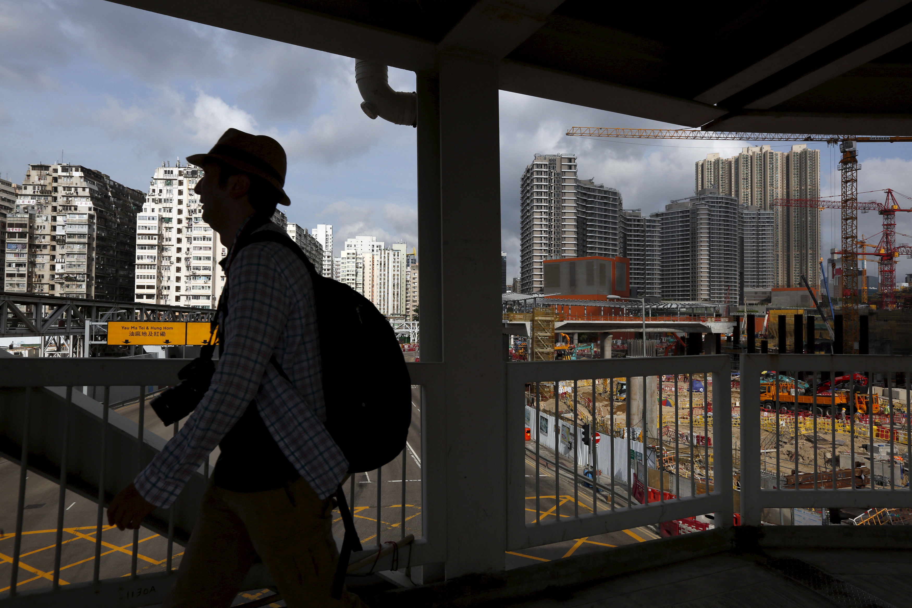 Man walks on a footbridge as 45-year-old residential flats, the latest luxury homes and a construction site are seen in the background, in West Kowloon, Hong Kong, China