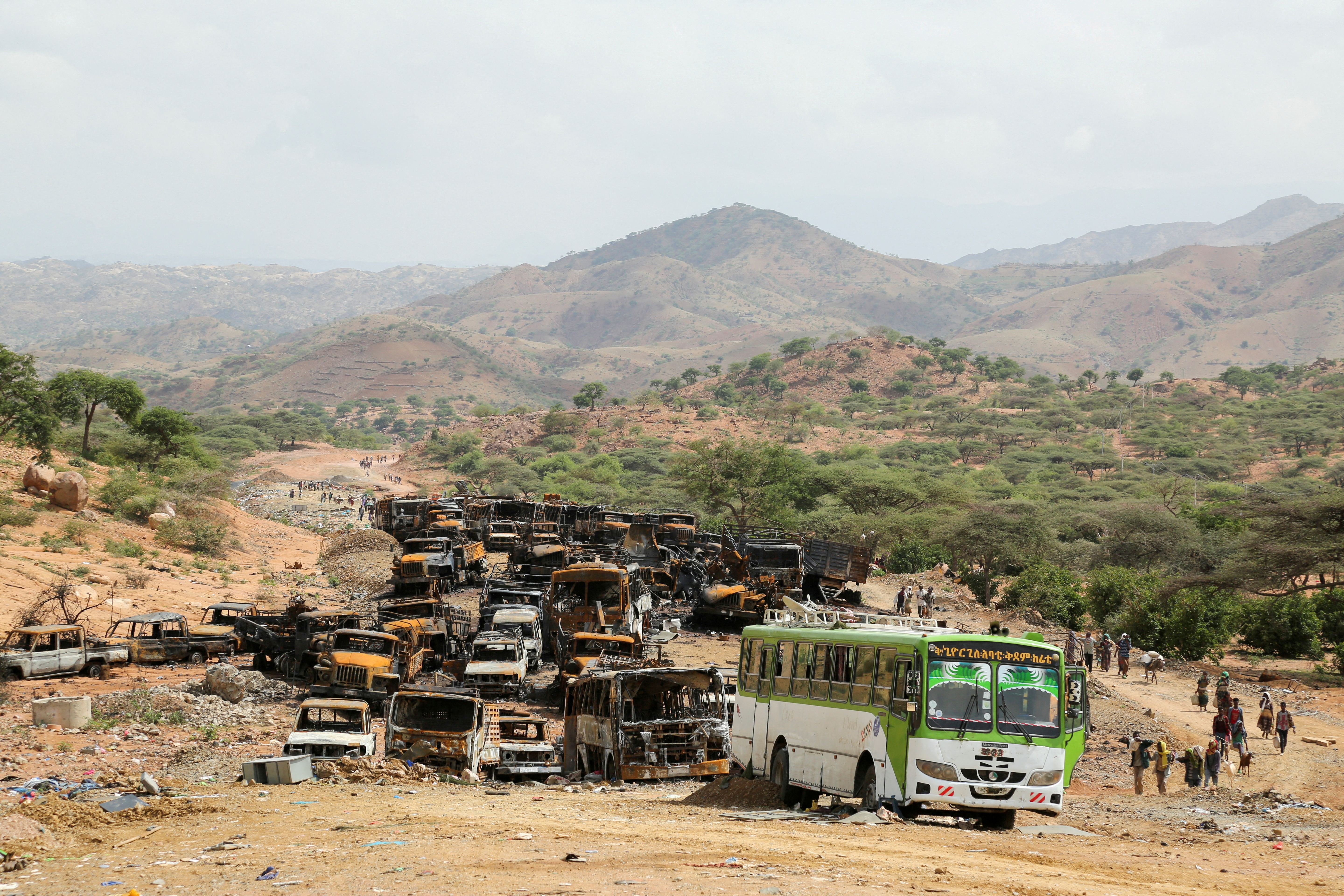 Villagers return from a market to Yechila town walking past scores of burned vehicles, in Tigray, Ethiopia