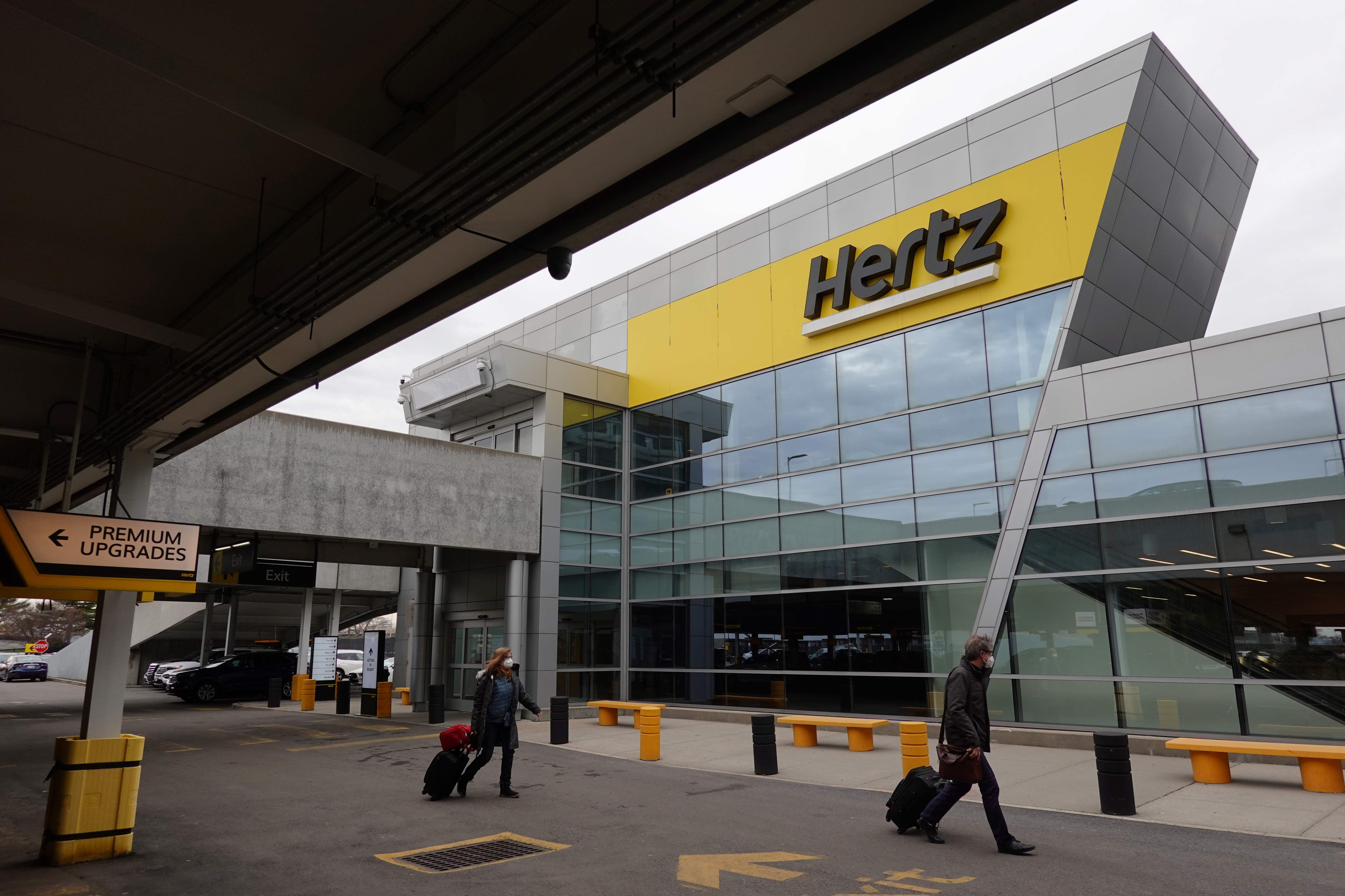 People walk by Hertz rental car signage at John F. Kennedy International Airport in Queens, New York City