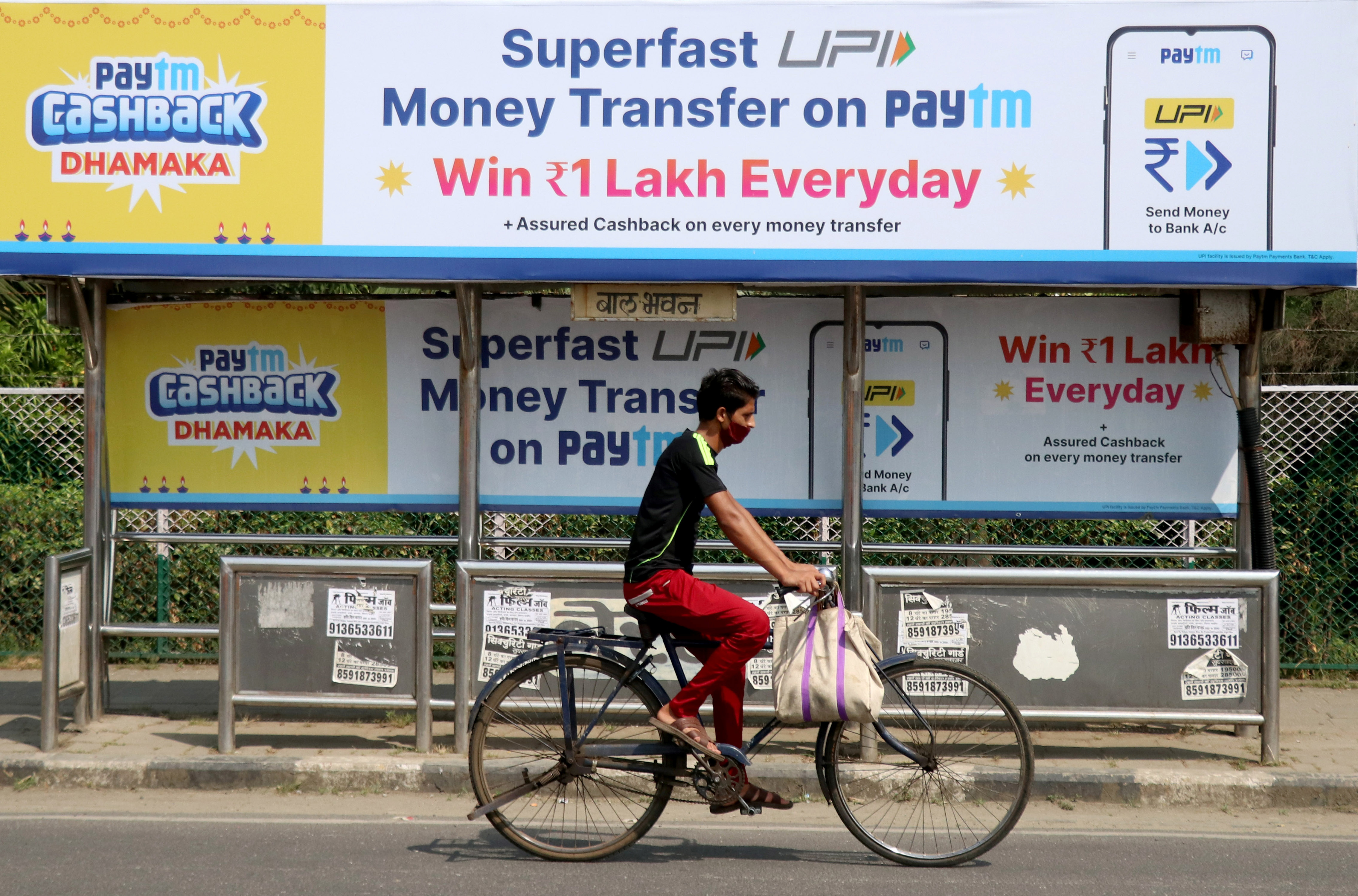 Man rides a bicycle past a bus stop with Paytm advertisements in Mumbai
