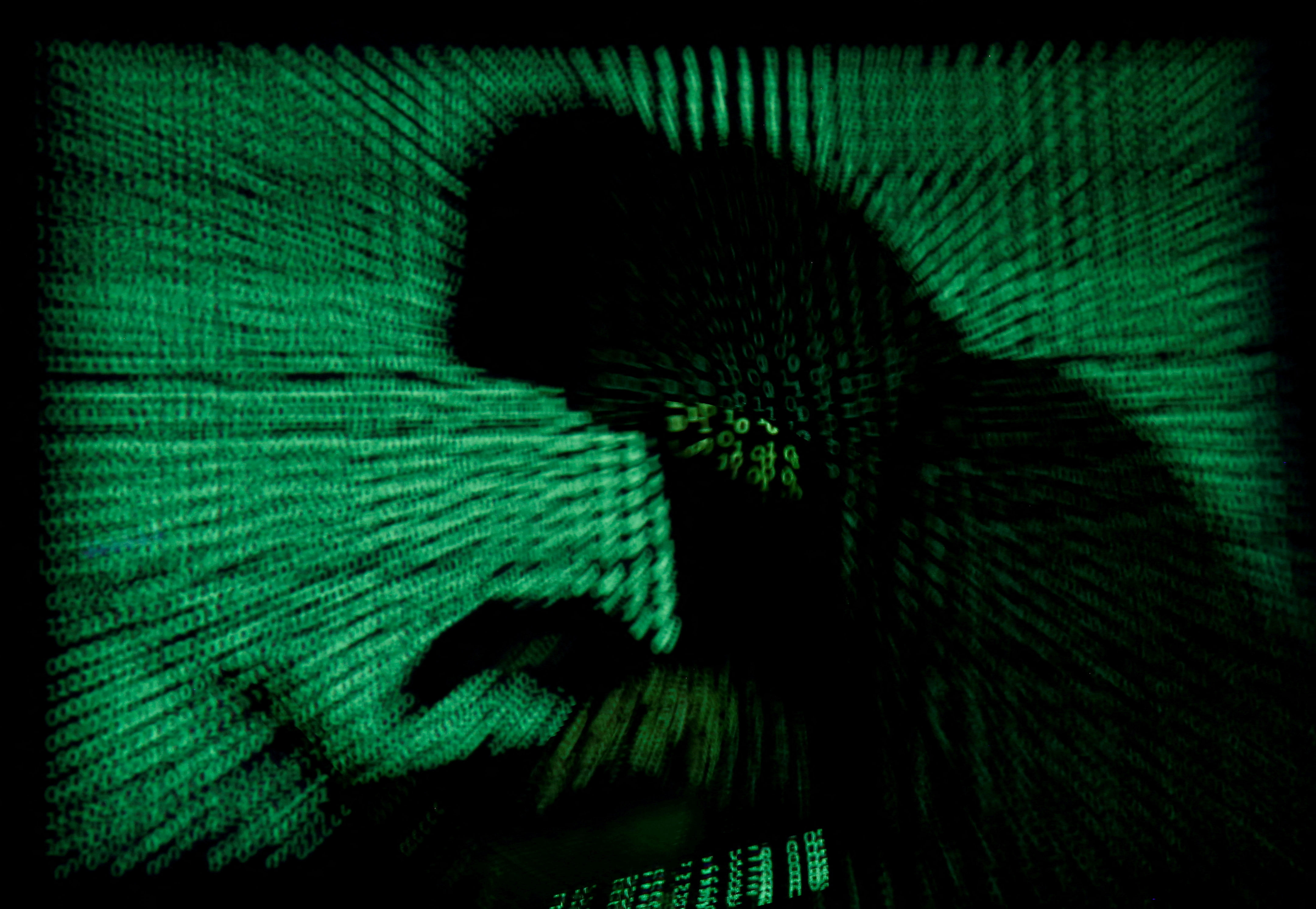 Hooded an holds laptop computer as cyber code is projected on him in this illustration picture