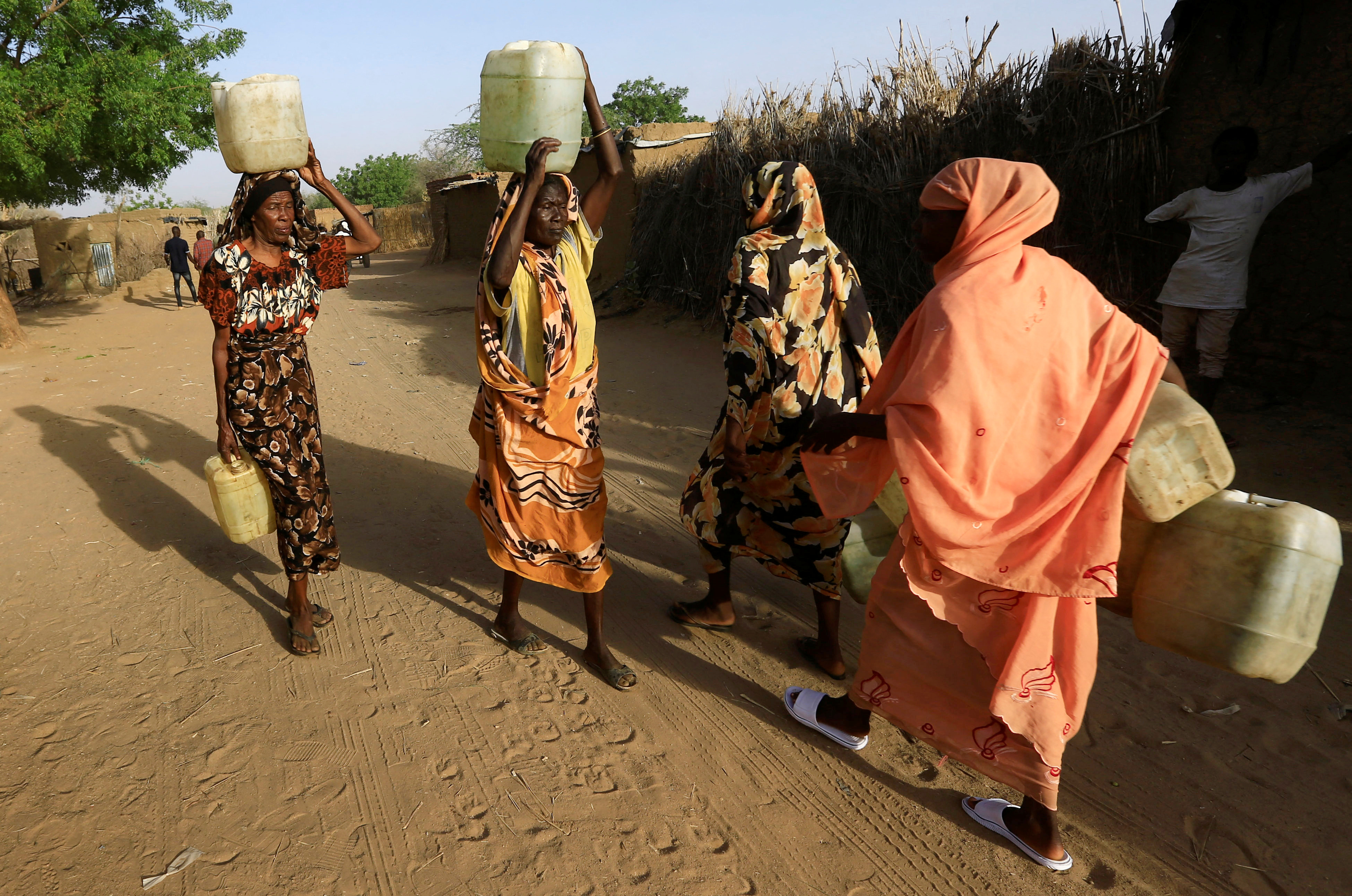 Internally displaced Sudanese women carry water from a tap within the Kalma camp for IDPs in Darfur