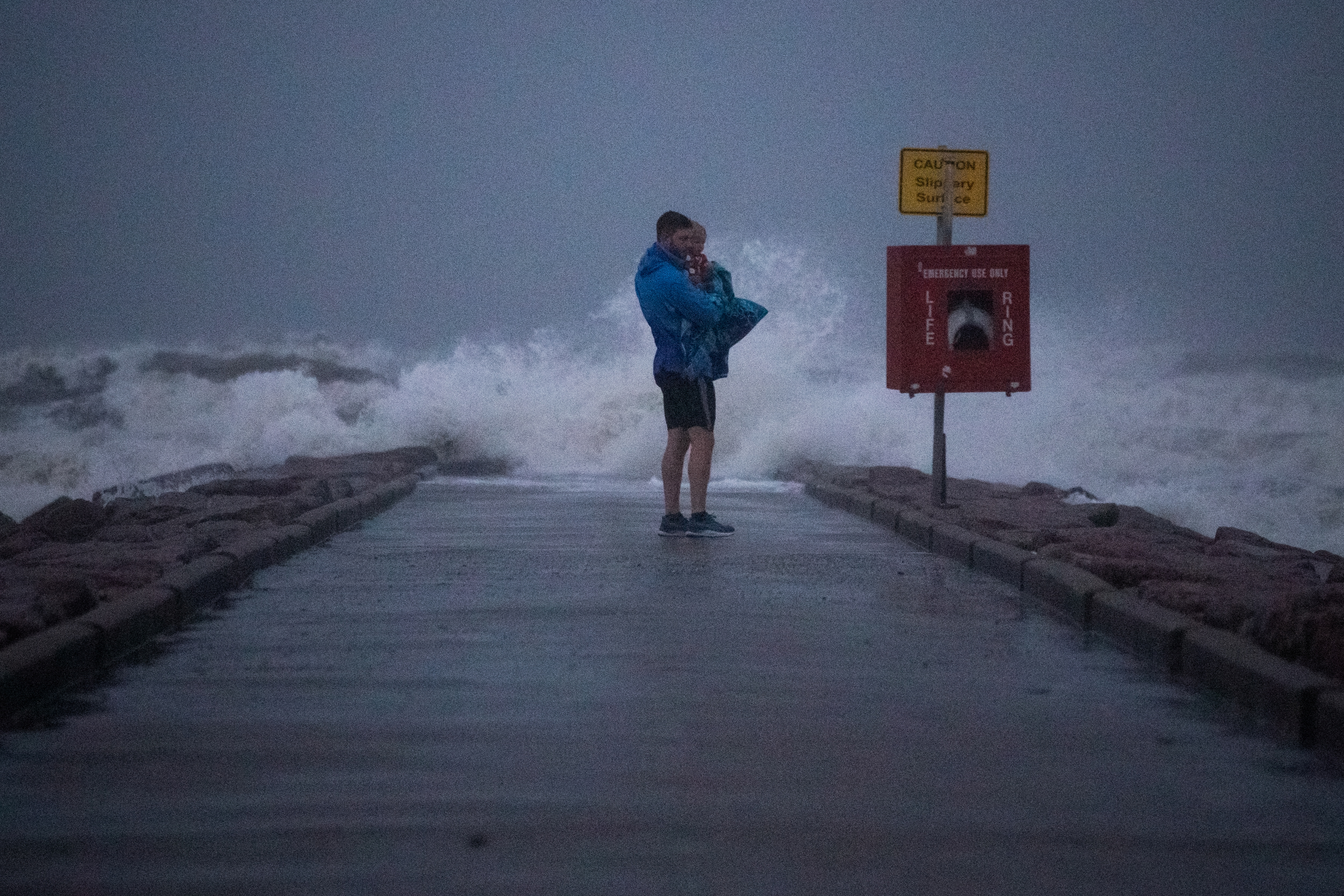 Local resident John Smith holds his 18-month-old son Owen as he stands near breaking waves on a pier ahead of the arrival of Tropical Storm Nicholas in Galveston, Texas, U.S., September 13, 2021. REUTERS/Adrees Latif