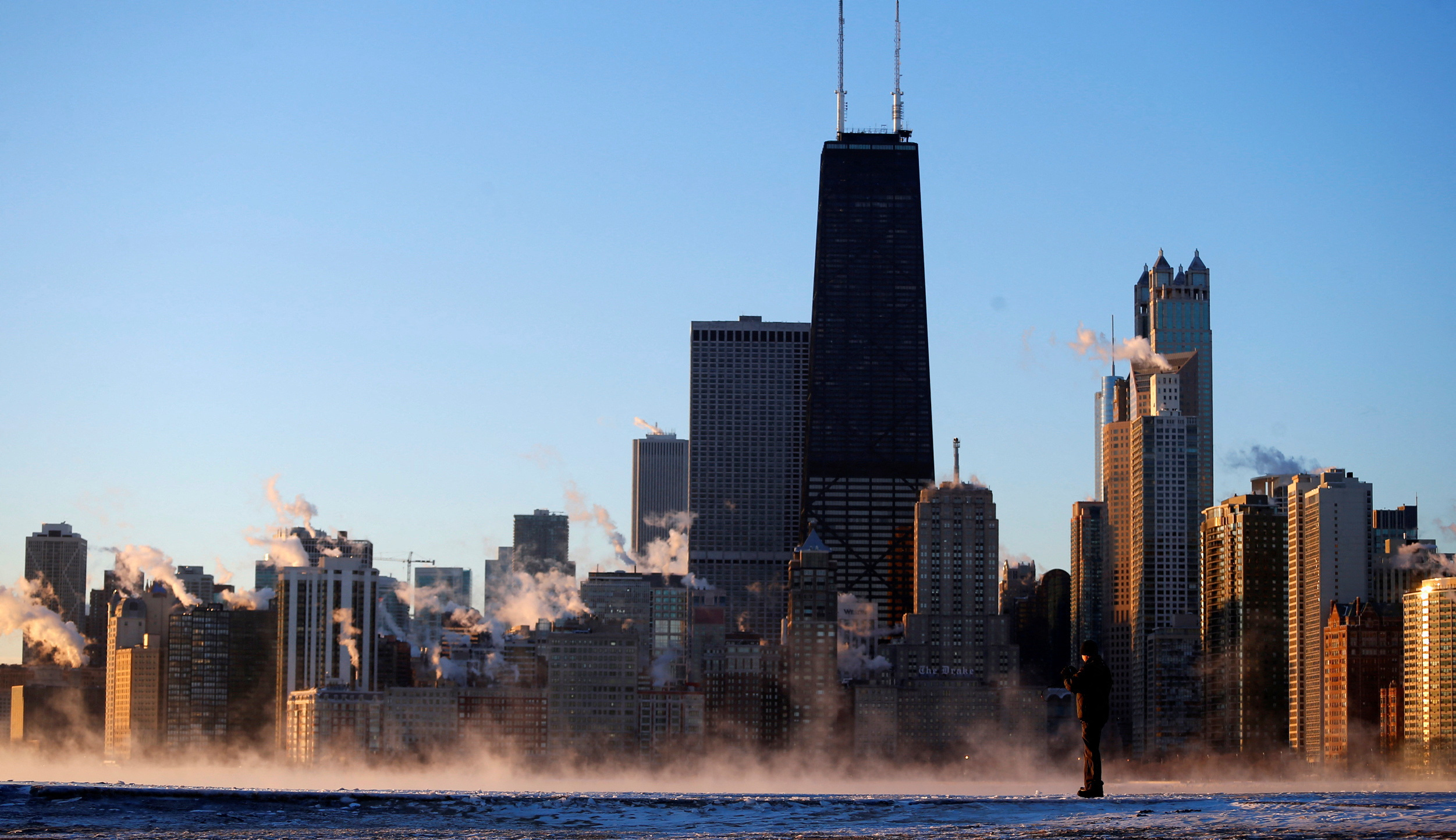 A man takes a picture against the Chicago skyline as the steam fog rises off Lake Michigan in Chicago, Illinois