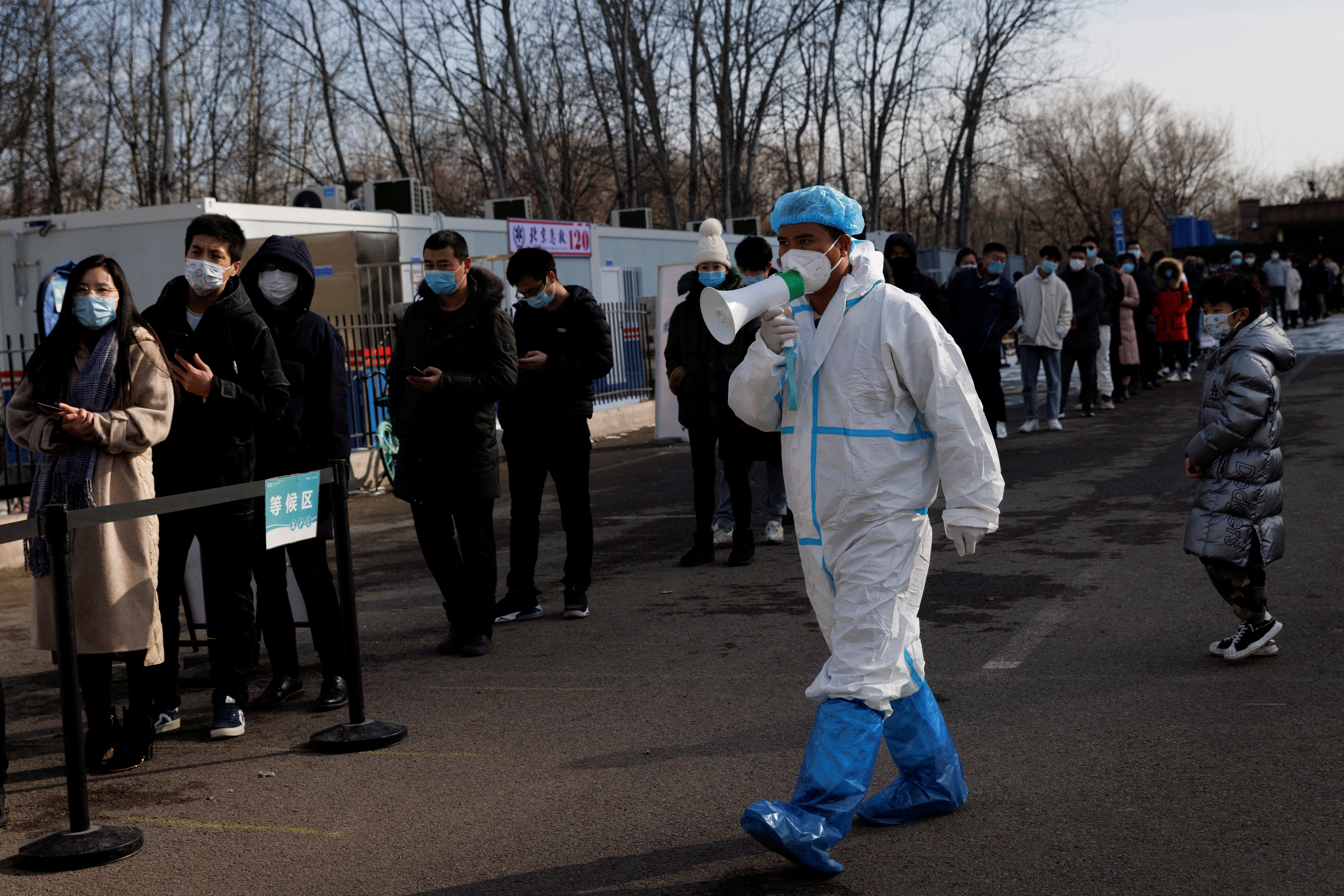 A staff member in a protective suit instructs people who are lining up for a throat swab test at a temporary COVID-19 testing center as the coronavirus disease (COVID-19) continues in Beijing
