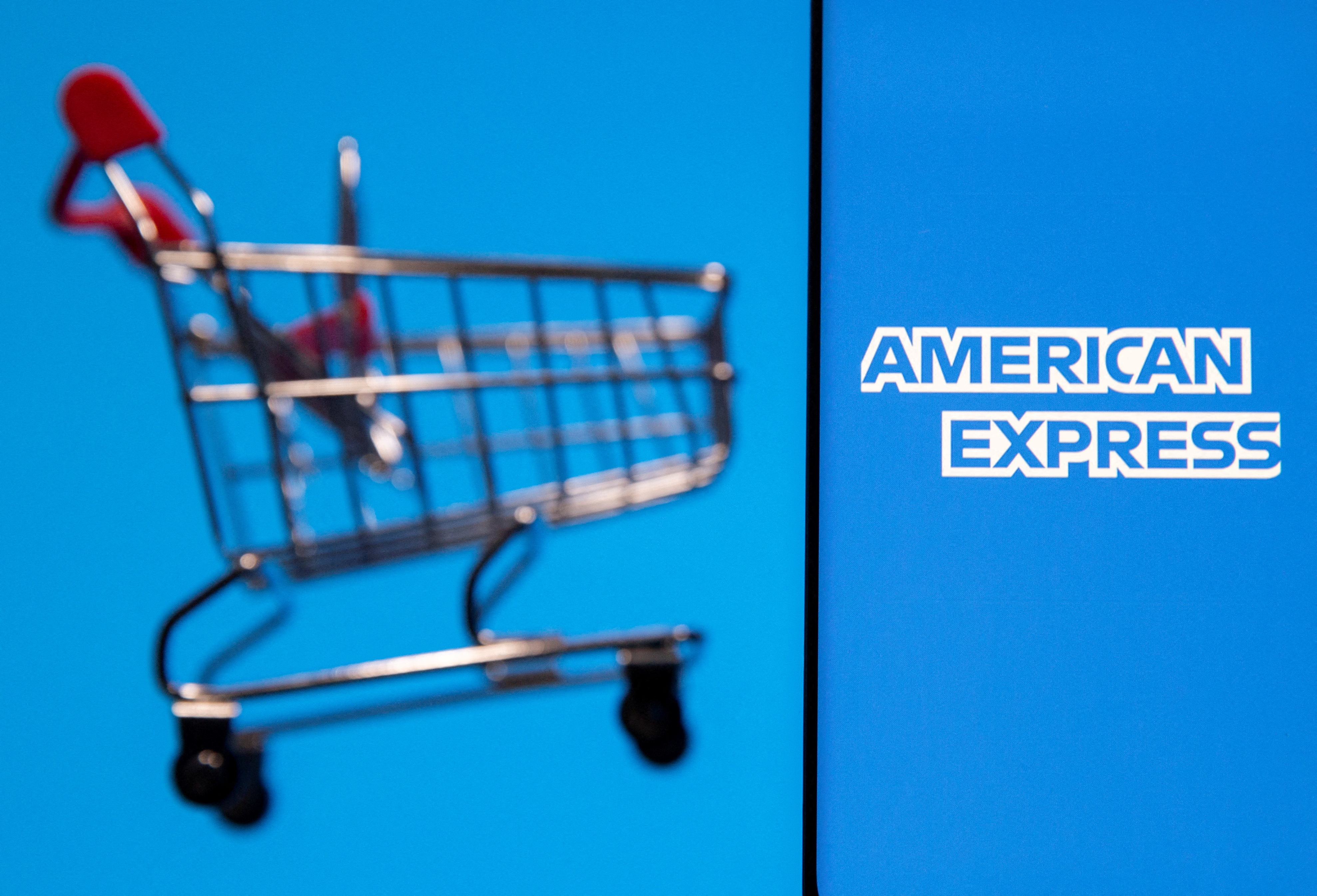 A smartphone with the American Express logo is placed near a toy shopping cart in this illustration