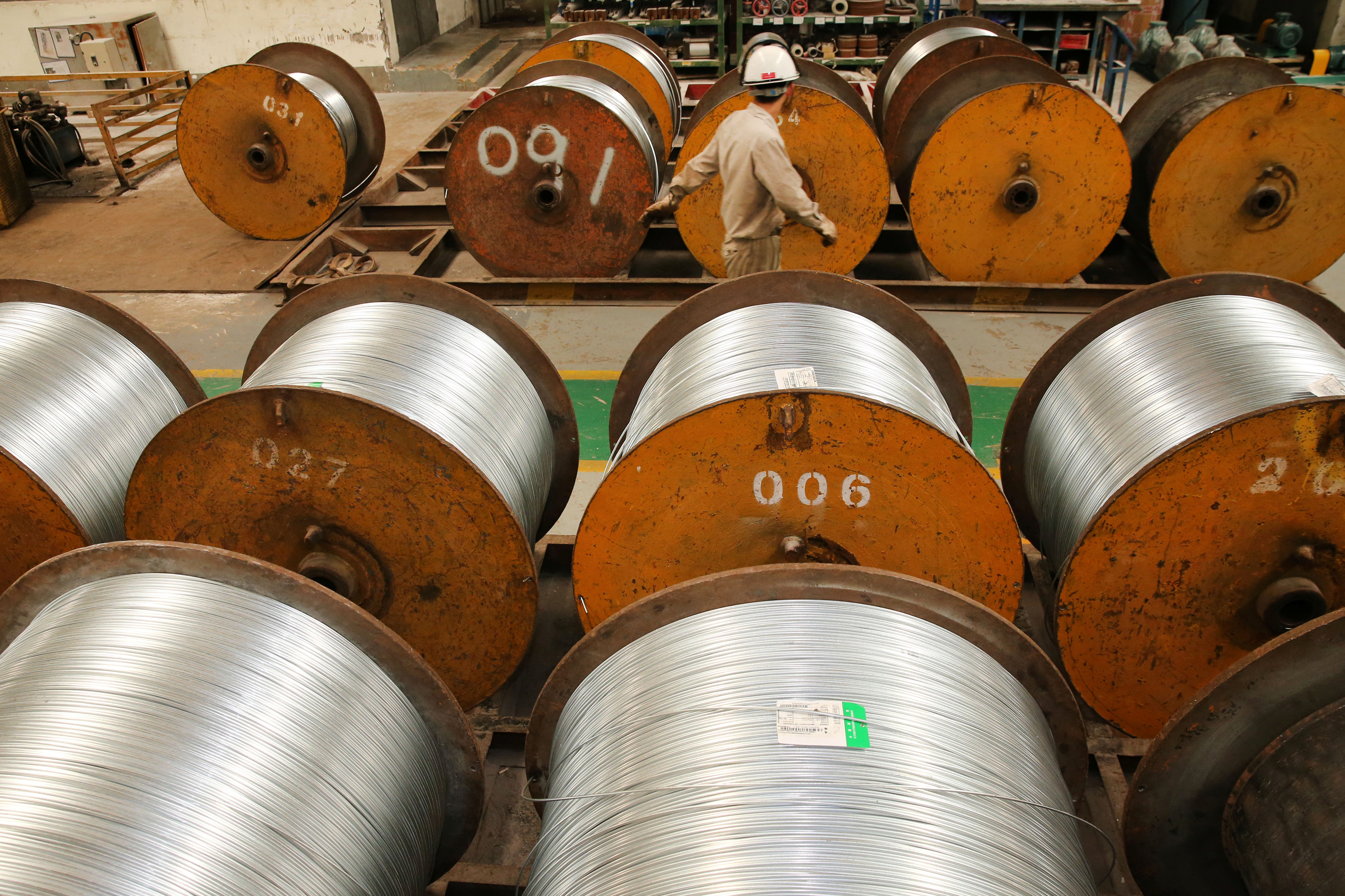 Worker walks past rolls of steel wires at a factory in Nantong, Jiangsu