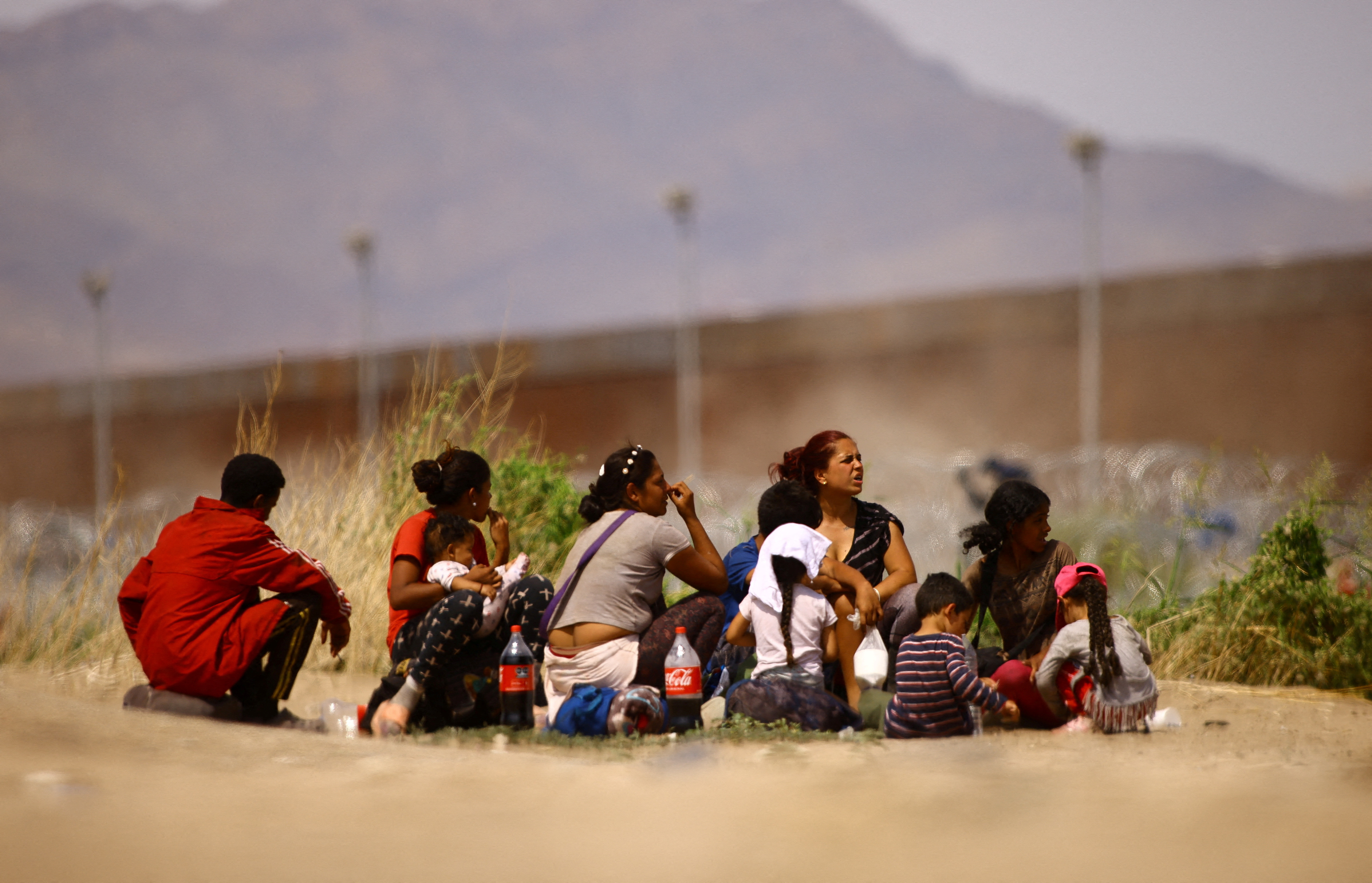 Migrants sit before crossing the Rio Bravo river, as seen from Ciudad Juarez