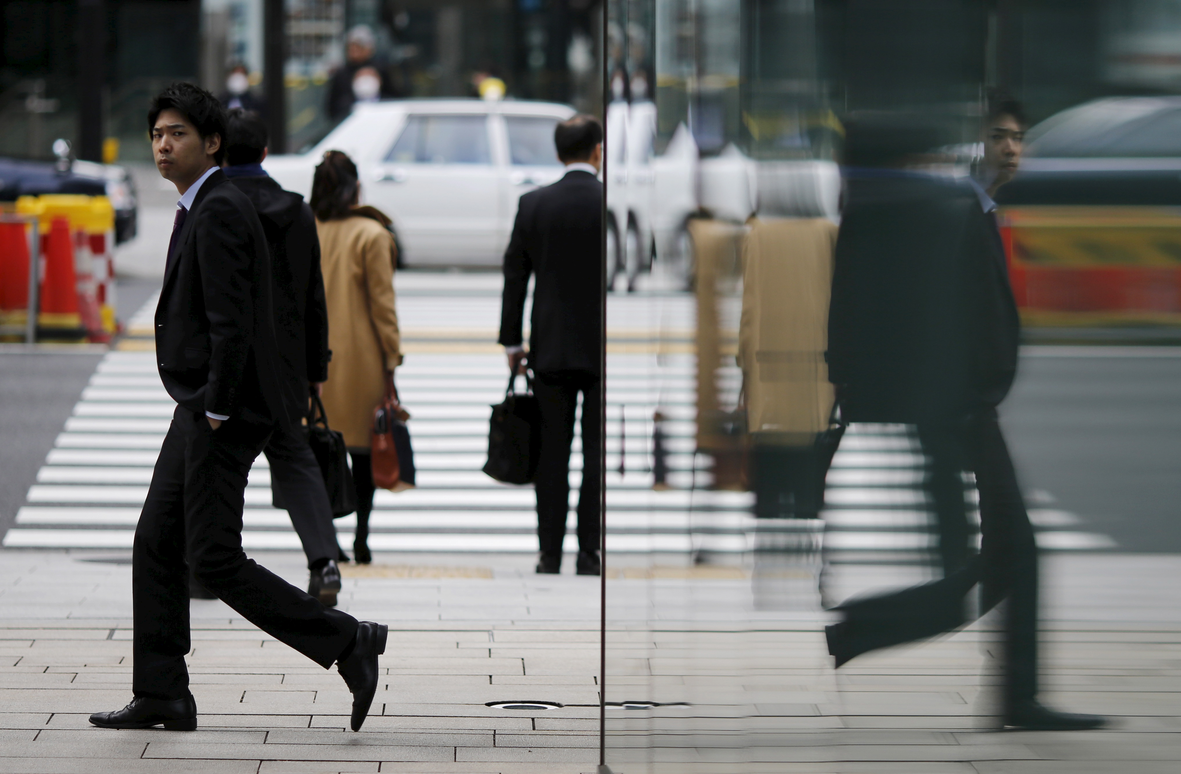 A businessman is reflected on a wall as he walks along Tokyo's business district, Japan