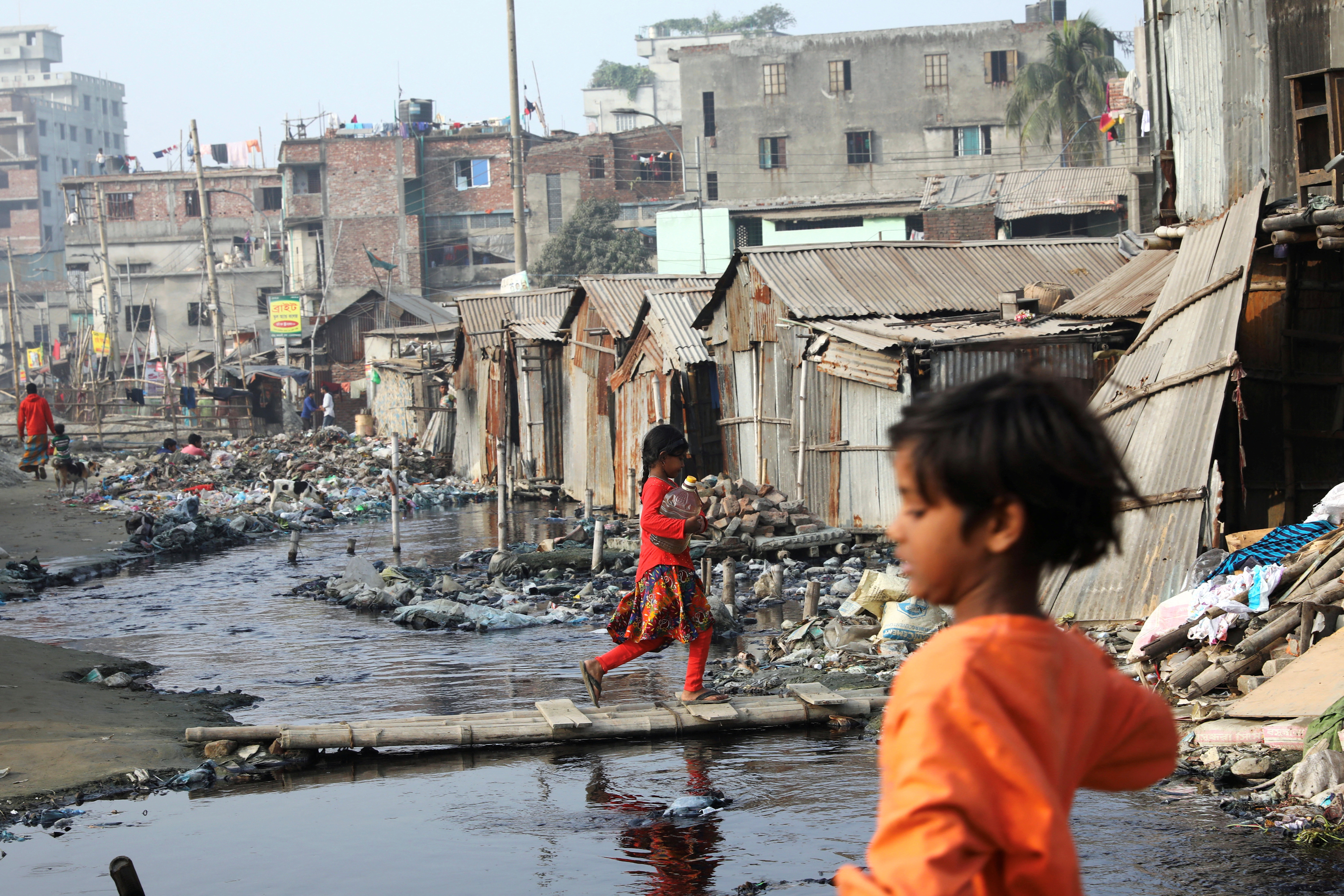 A girl carries a water bottle in a polluted slum area in Dhaka