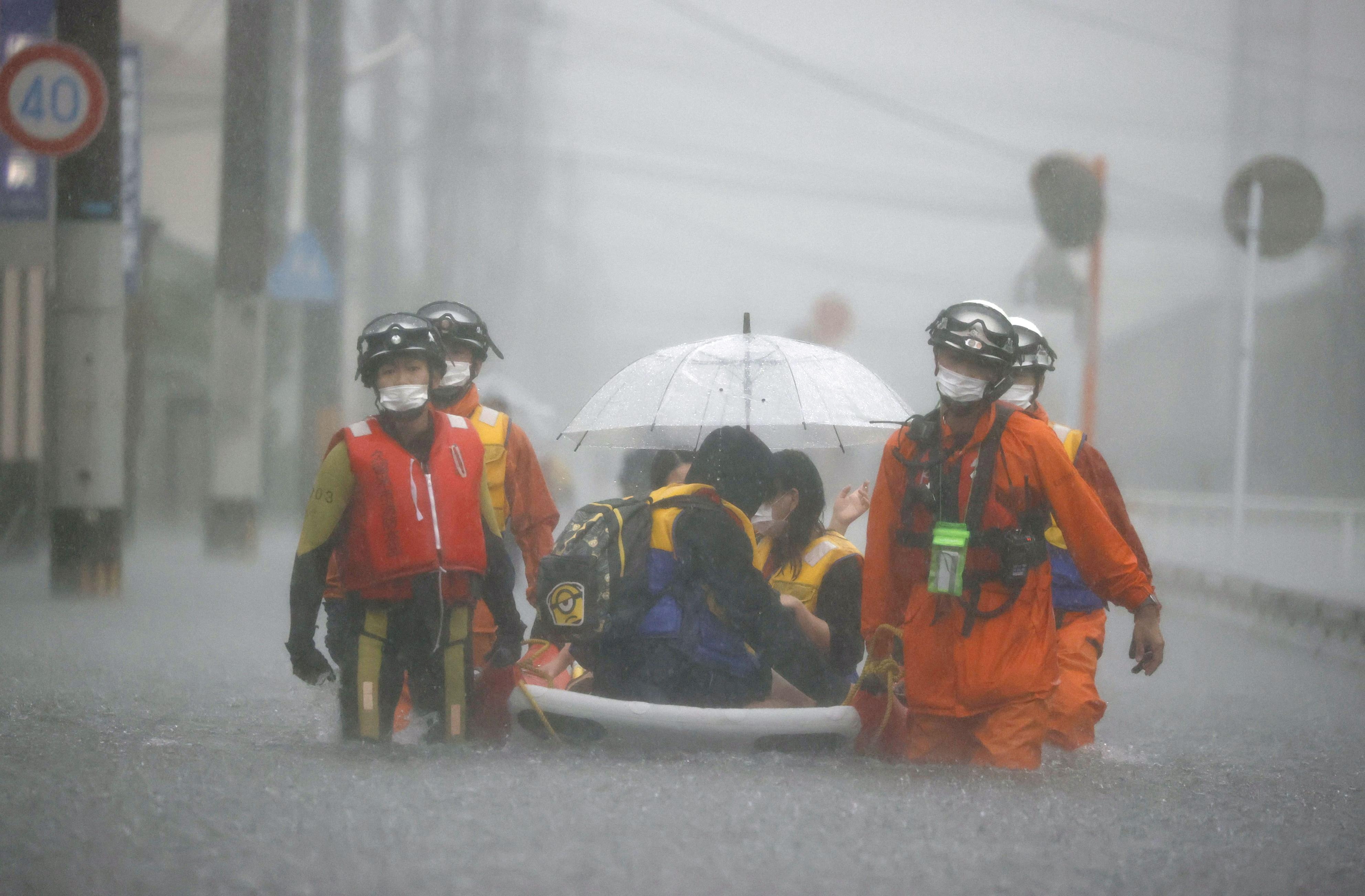 Firefighters transport stranded residents on a boat in a road flooded by heavy rain in Kurume, Japan