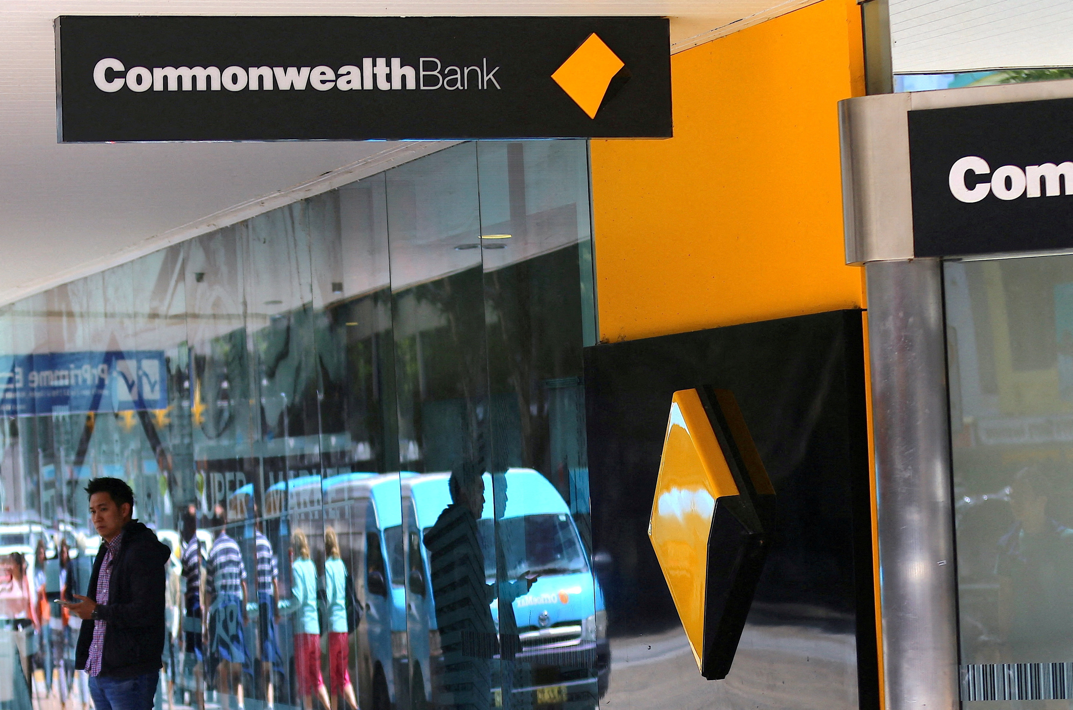 A pedestrian is reflected in the window of a branch of the Commonwealth Bank of Australia (CBA) in Sydney, Australia