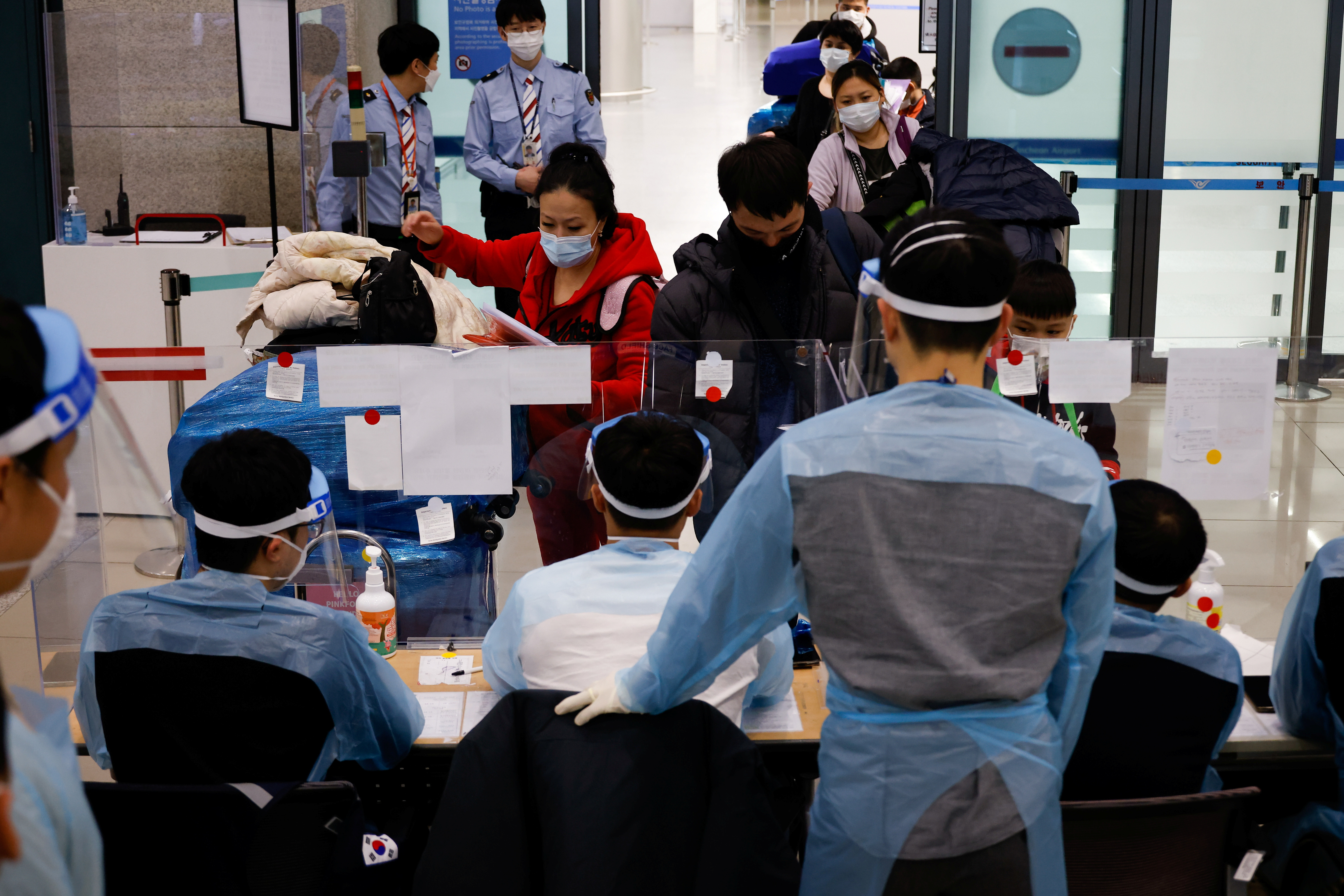 Workers wearing protective gear check passengers from overseas as they arrive at the Incheon International Airport, in Incheon