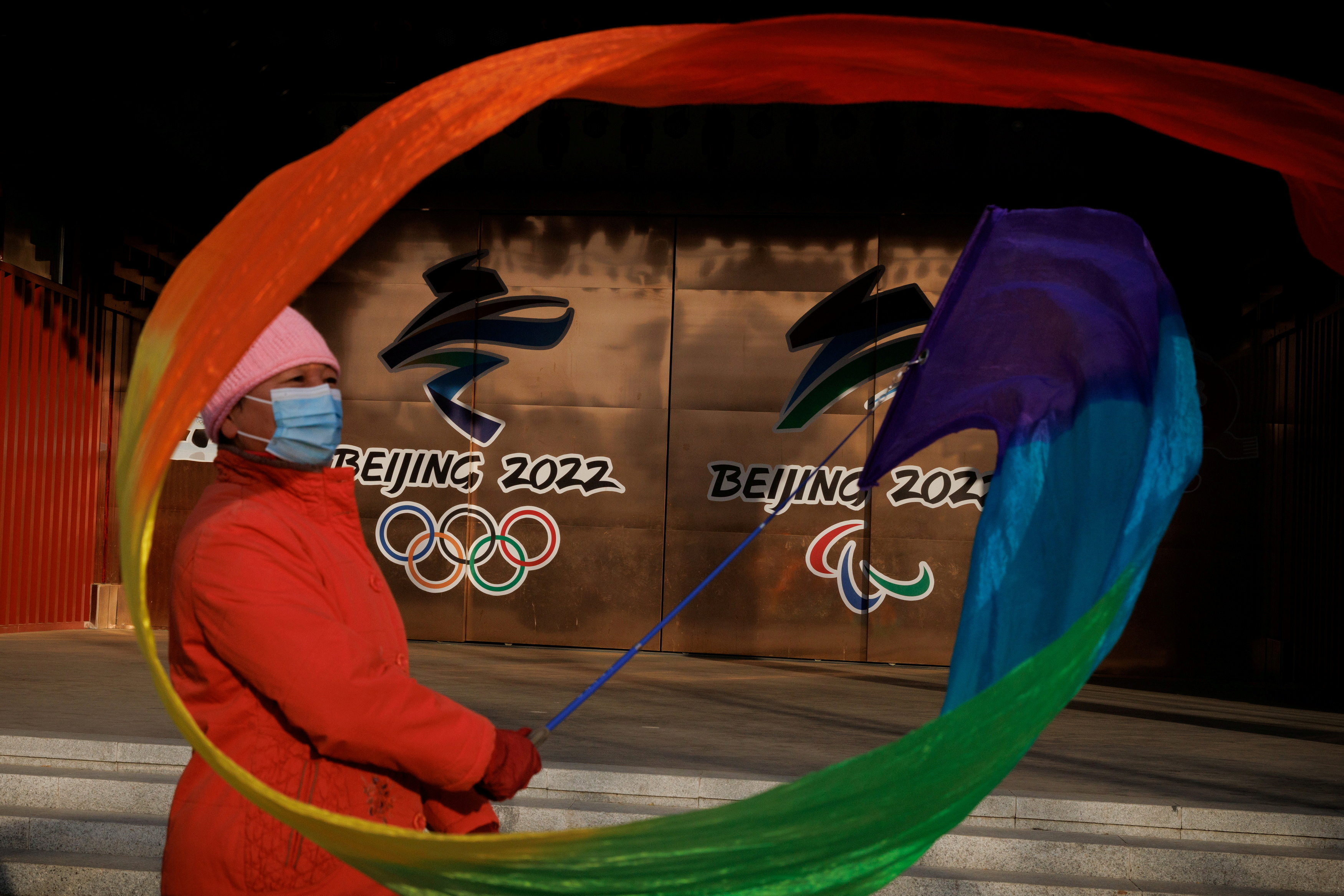 A woman flies a ribbon near the logos of the Beijing 2022 Olympic and Paralympic Games in a park in Beijing