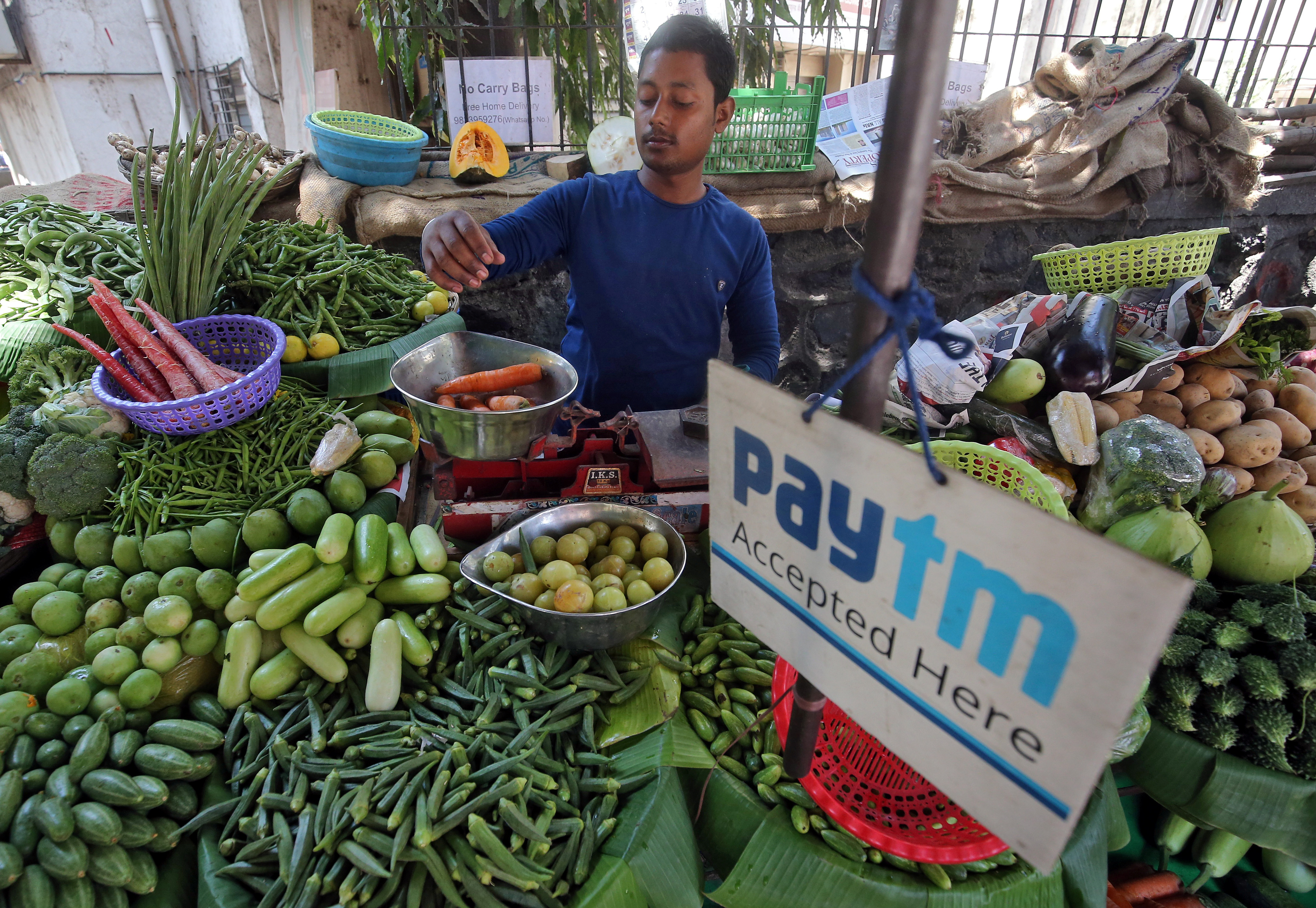 A vendor weighs vegetable next to an advertisement of Paytm, a digital payments firm, hanging amidst his vegetables at a roadside market in Mumbai
