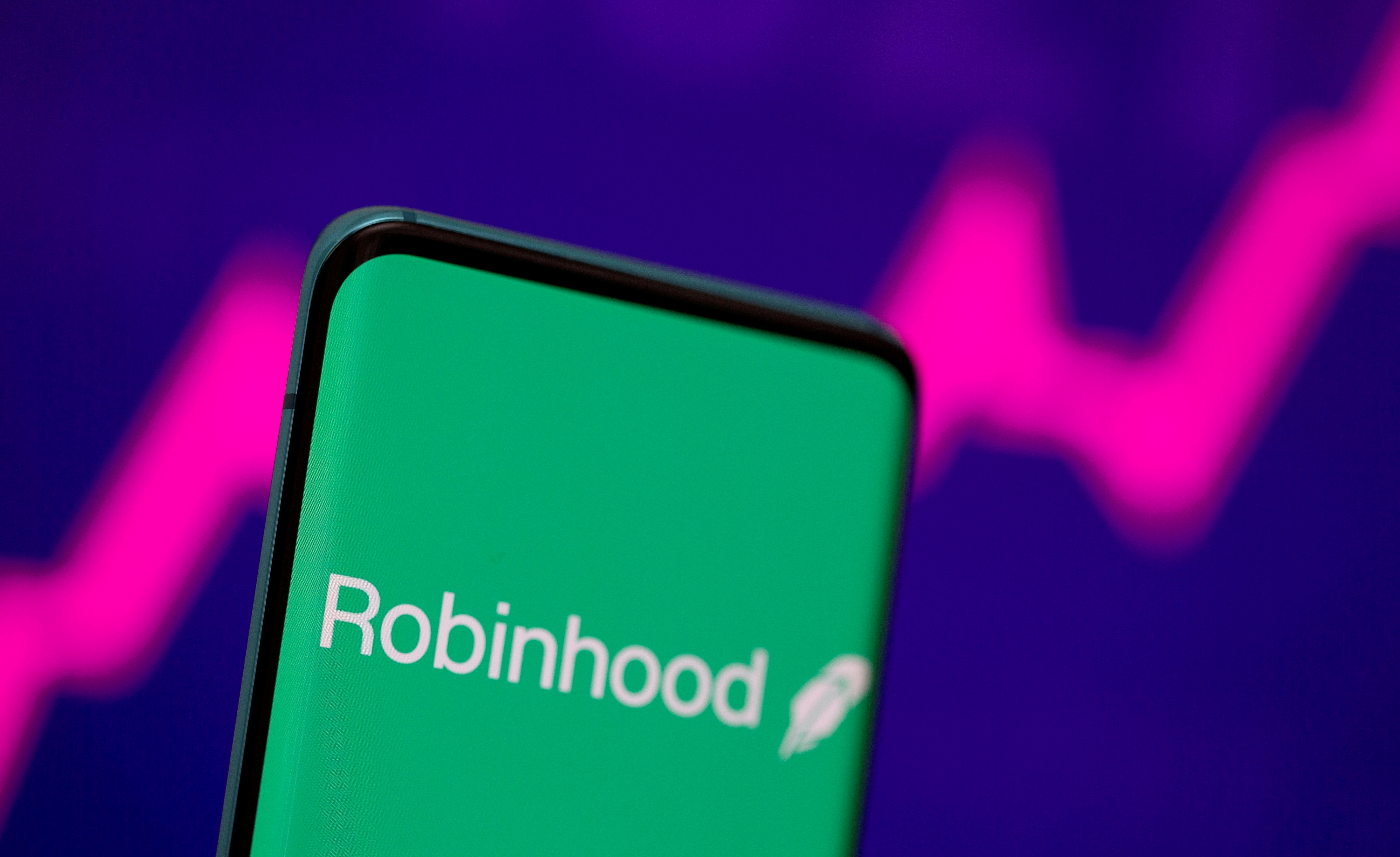 Robinhood logo is seen on a smartphone in front of a displayed stock graph in this illustration taken