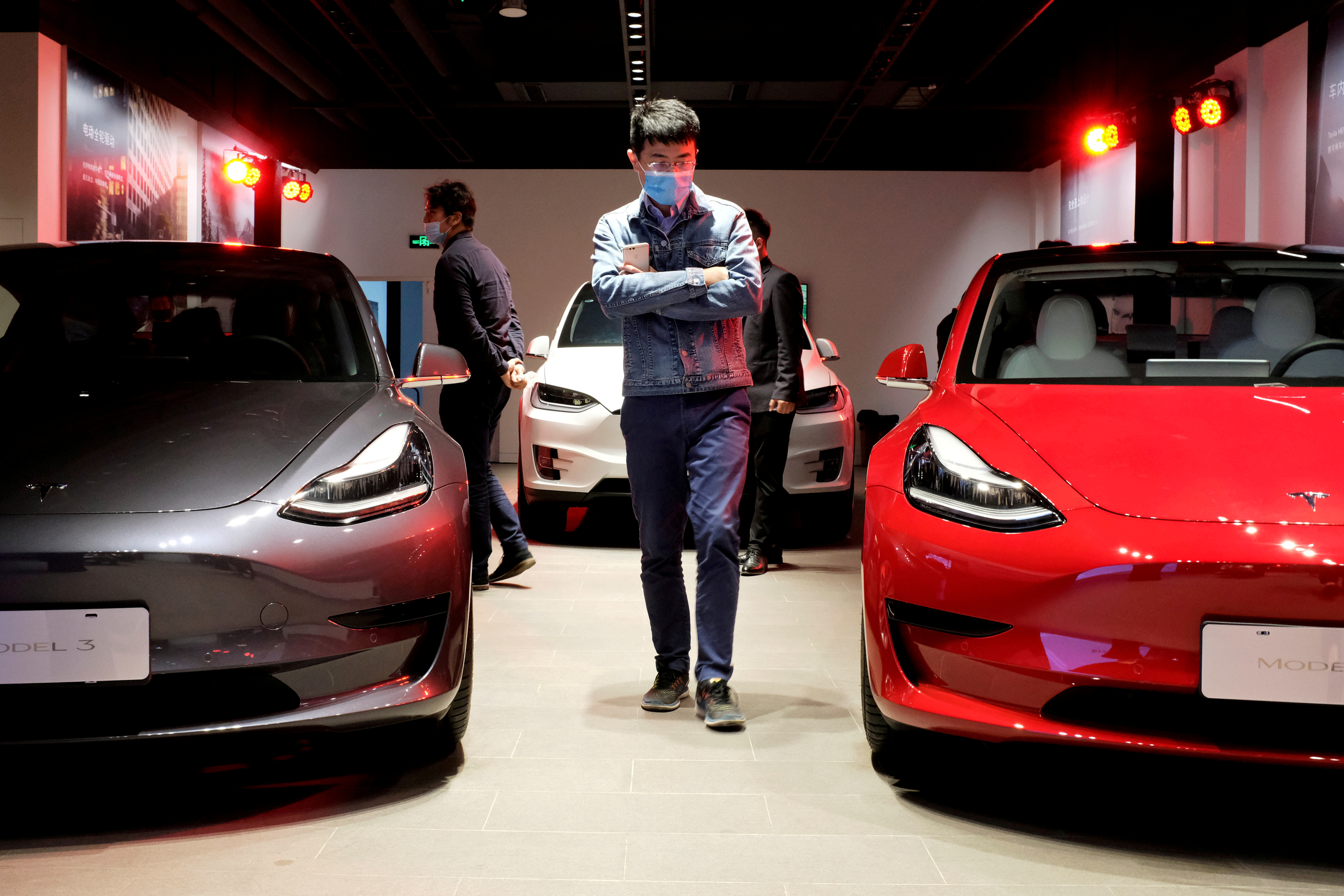 A man wearing a face mask following the coronavirus disease (COVID-19) outbreak walks by Tesla Model 3 sedans and Tesla Model X sport utility vehicle at a new Tesla showroom in Shanghai, China May 8, 2020. 
