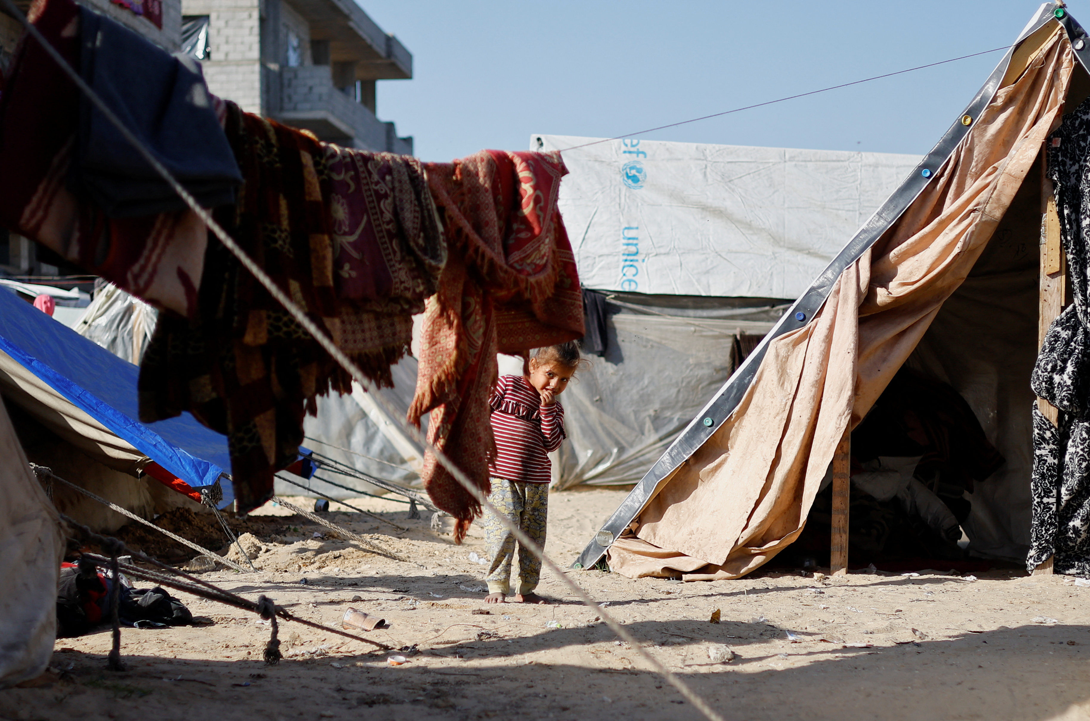 A displaced Palestinian child, who fled their house due to Israeli strikes, looks on inside a tent camp