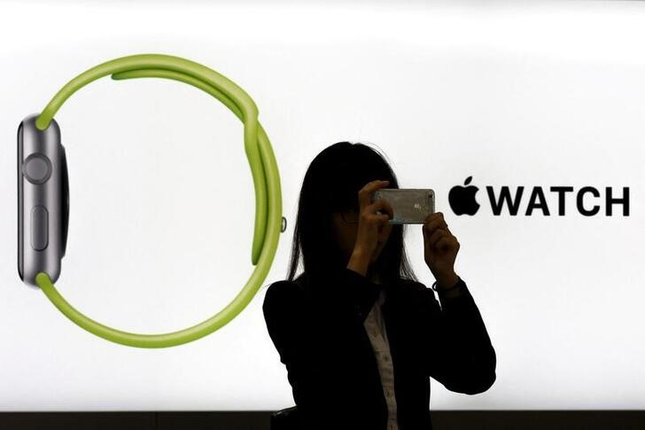 Woman takes pictures with smart phone as she stands in front of Apple Watch display at electronics store in Tokyo