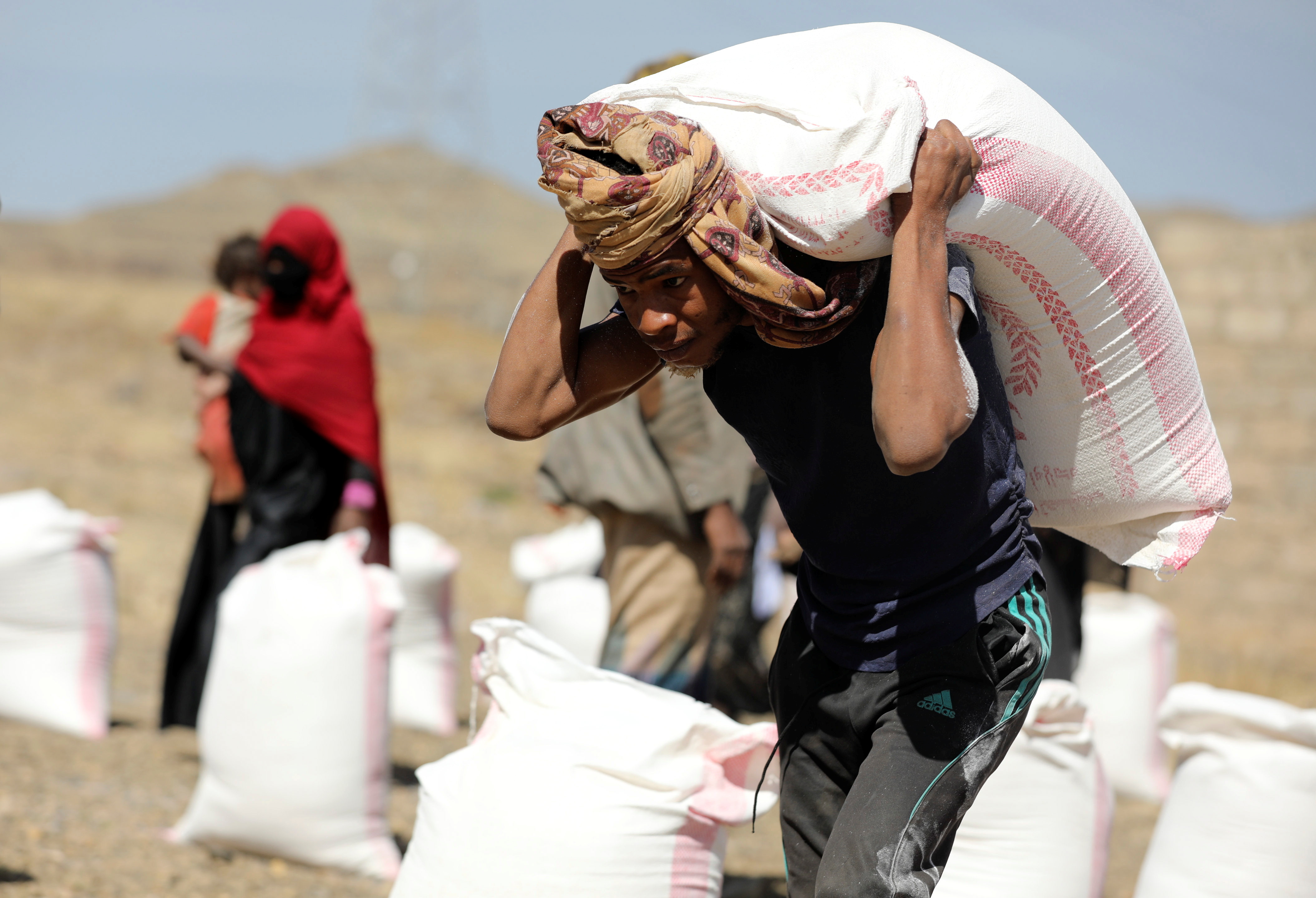 Worker carries a sack of wheat flour provided by the local charity Mona Relief to beneficiaries at a camp for internally displaced people on the outskirts of Sanaa