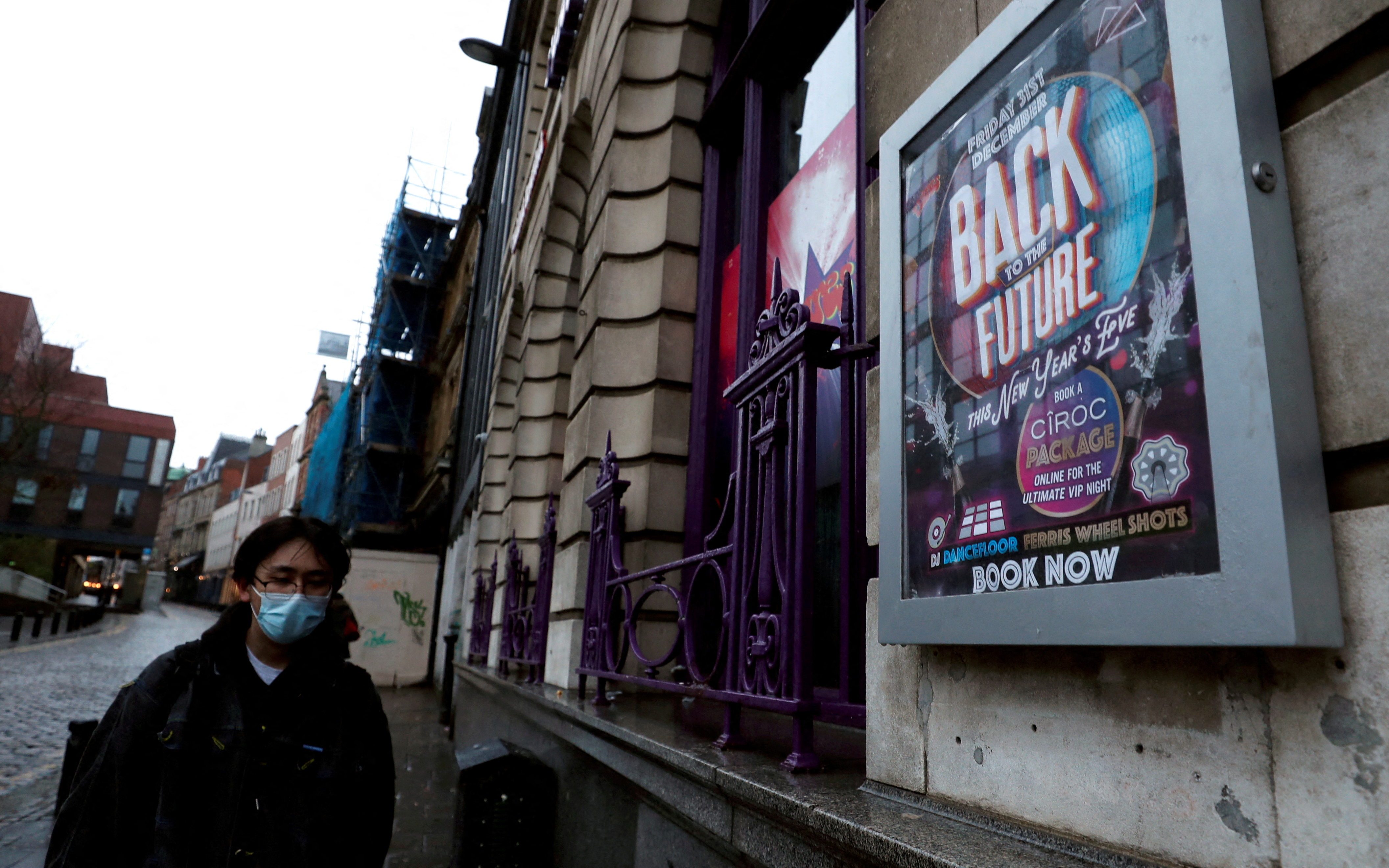 Man in a face mask walks past a New Year's Eve advertisement at Flares Bar in Newcastle upon Tyne