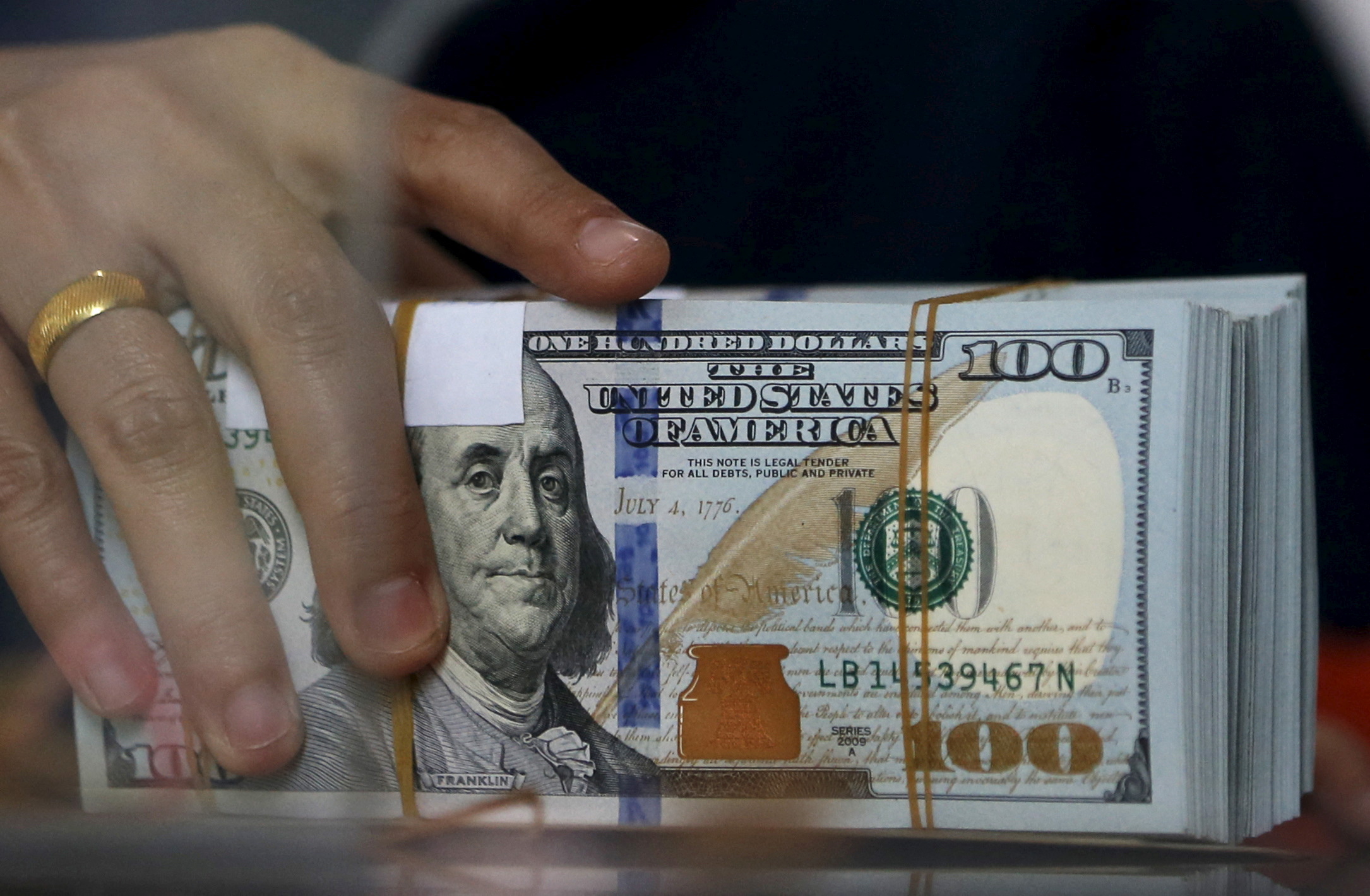 An employee of a money changer holds a stack of U.S. dollar notes before giving it to a customer in Jakarta