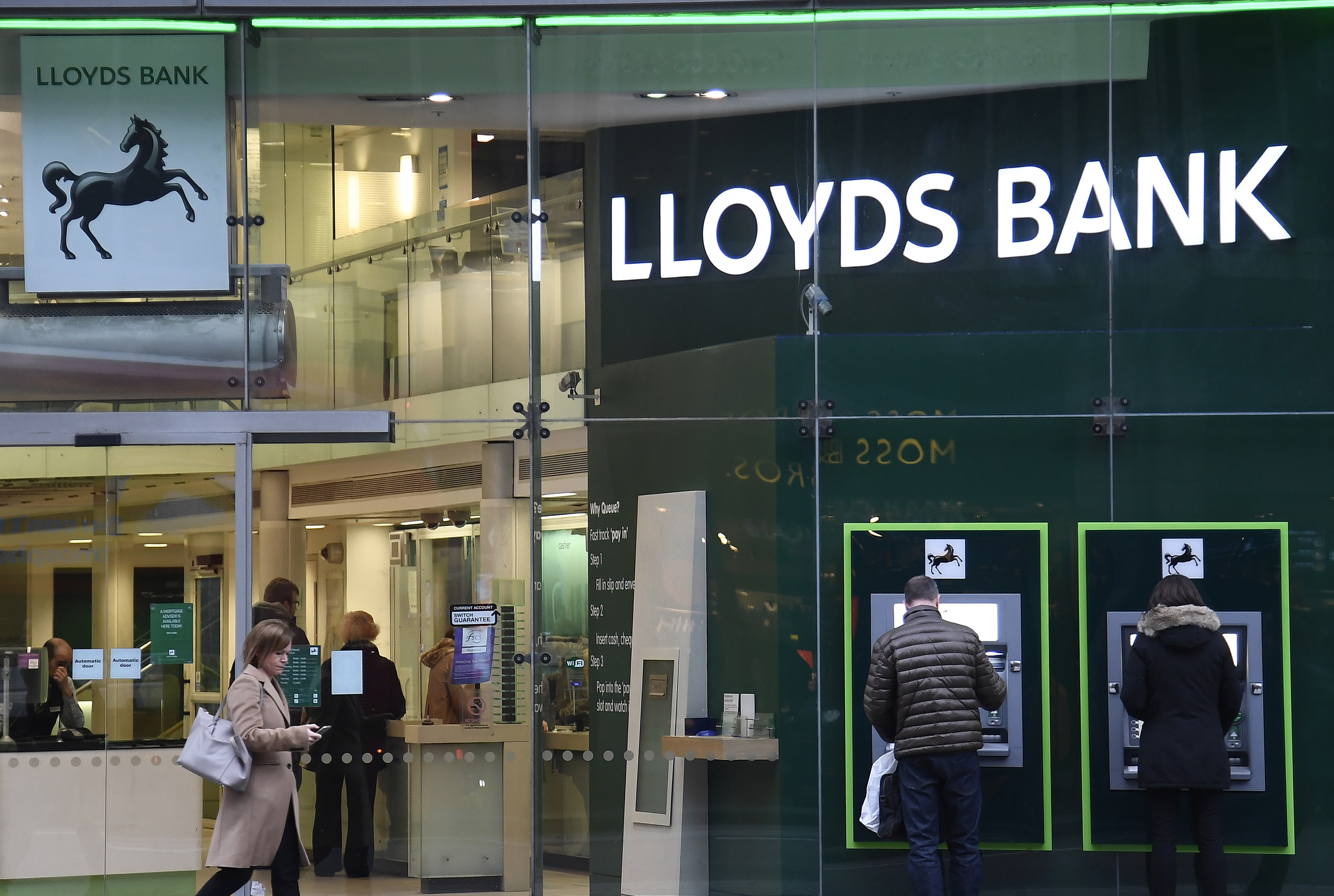 Customers use ATMs at a branch of Lloyds Bank in London