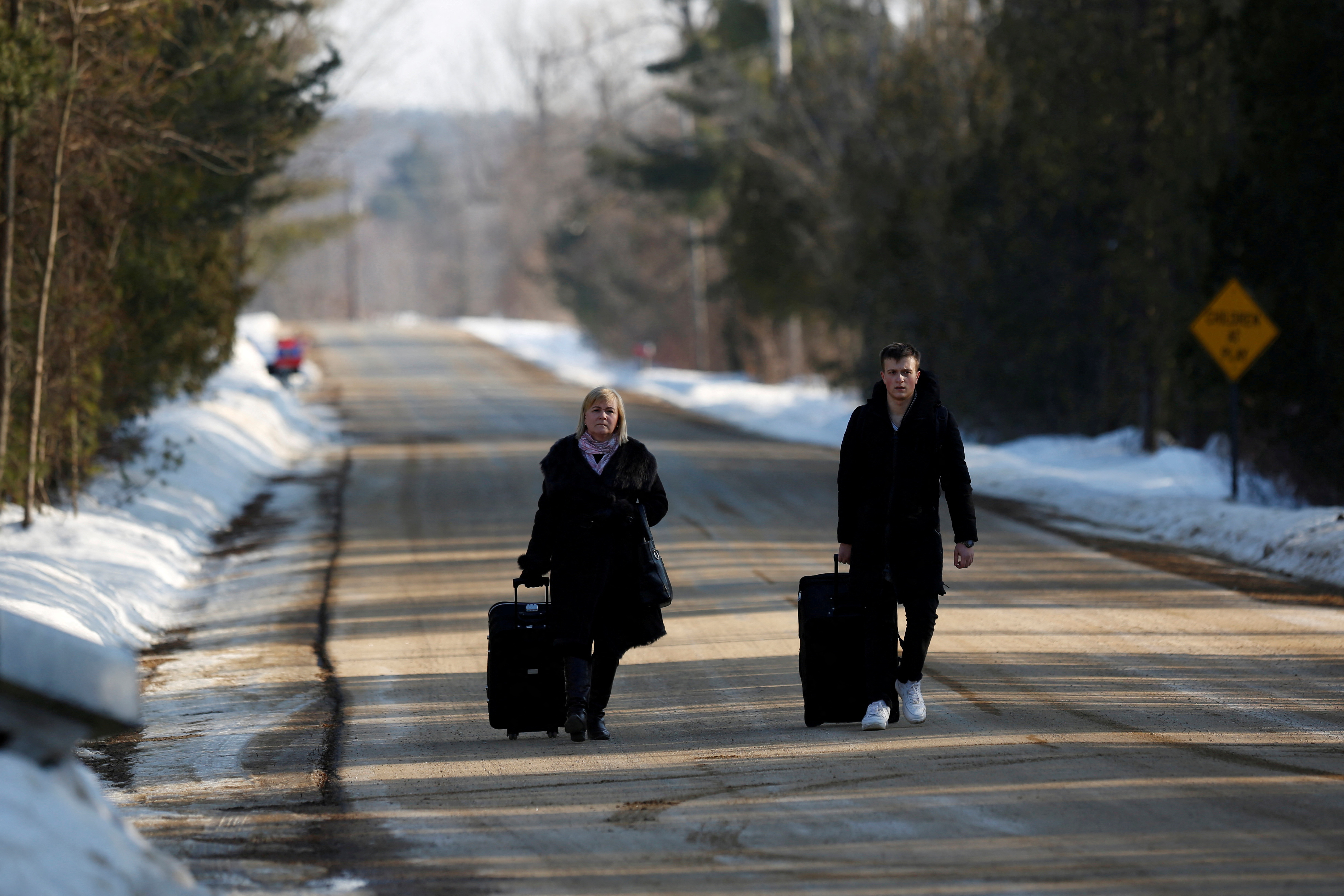 People walk with their luggage on Roxham Road before crossing the US-Canada in Champlain