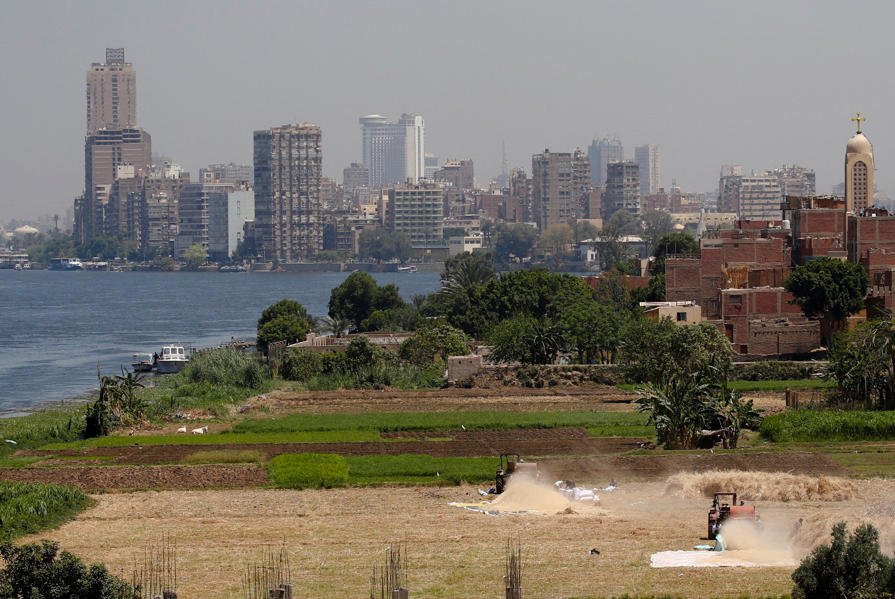 Farmers use a threshing machine as they harvest their wheat crop at a farmland on an island on the River Nile next to the capital city of Cairo