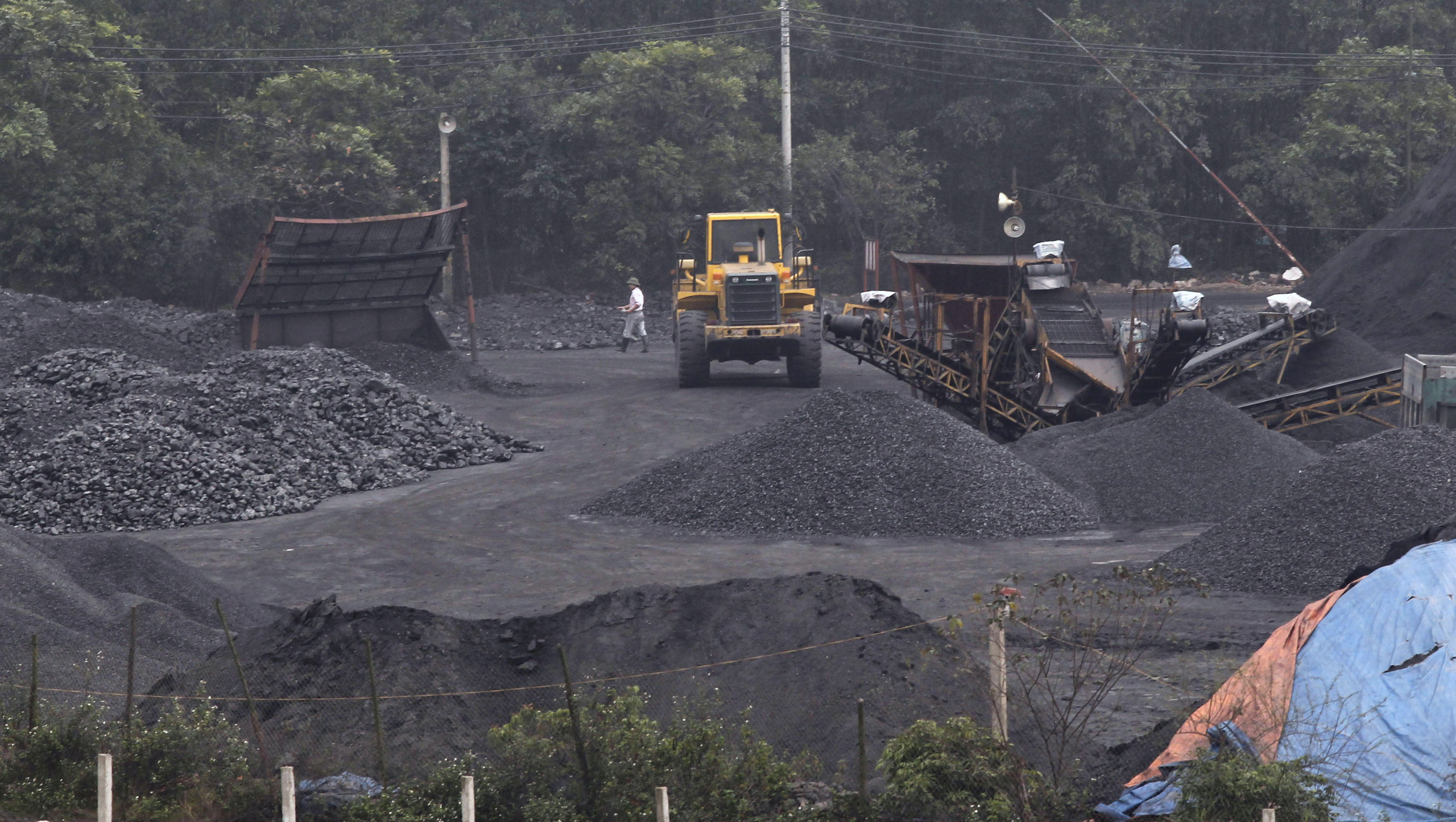 Workers walk near an excavator loading coal onto a truck at a coal port in Hanoi