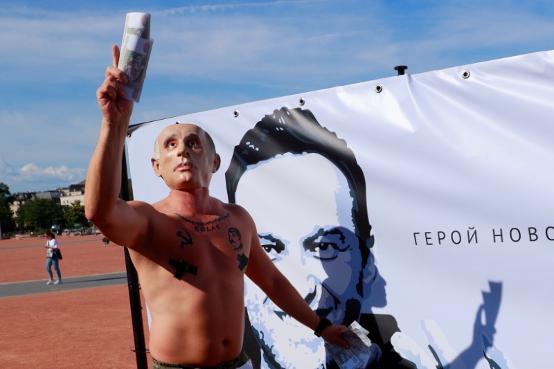 A protester wearing a mask of Russian President Vladimir Putin holds fake bank notes as he stands  in front of a poster of Alexei Navalny ahead of a meeting between U.S. President Joe Biden and Russian President Vladimir Putin in Geneva