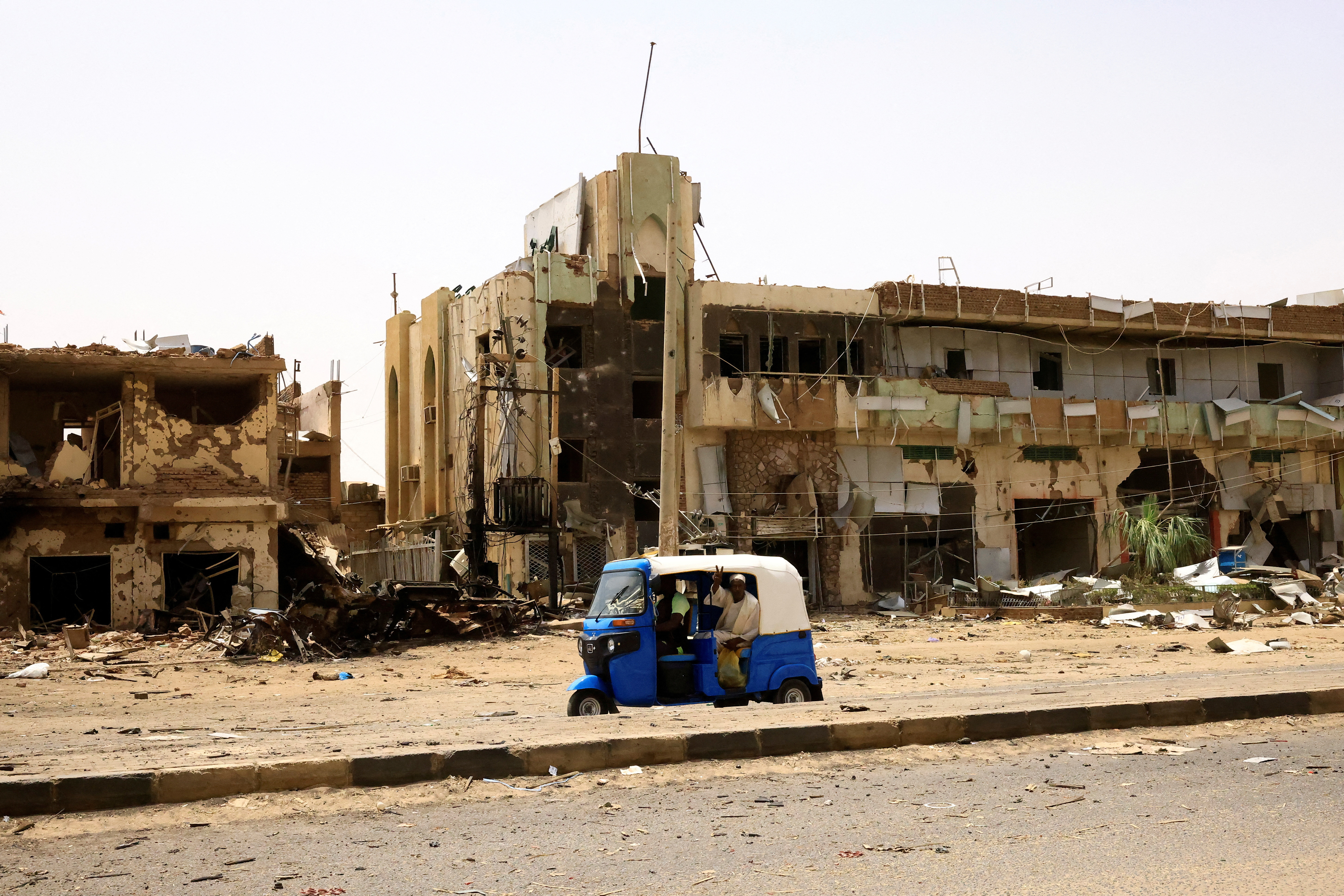 People pass by damaged cars and buildings at the Central Market in North Khartoum