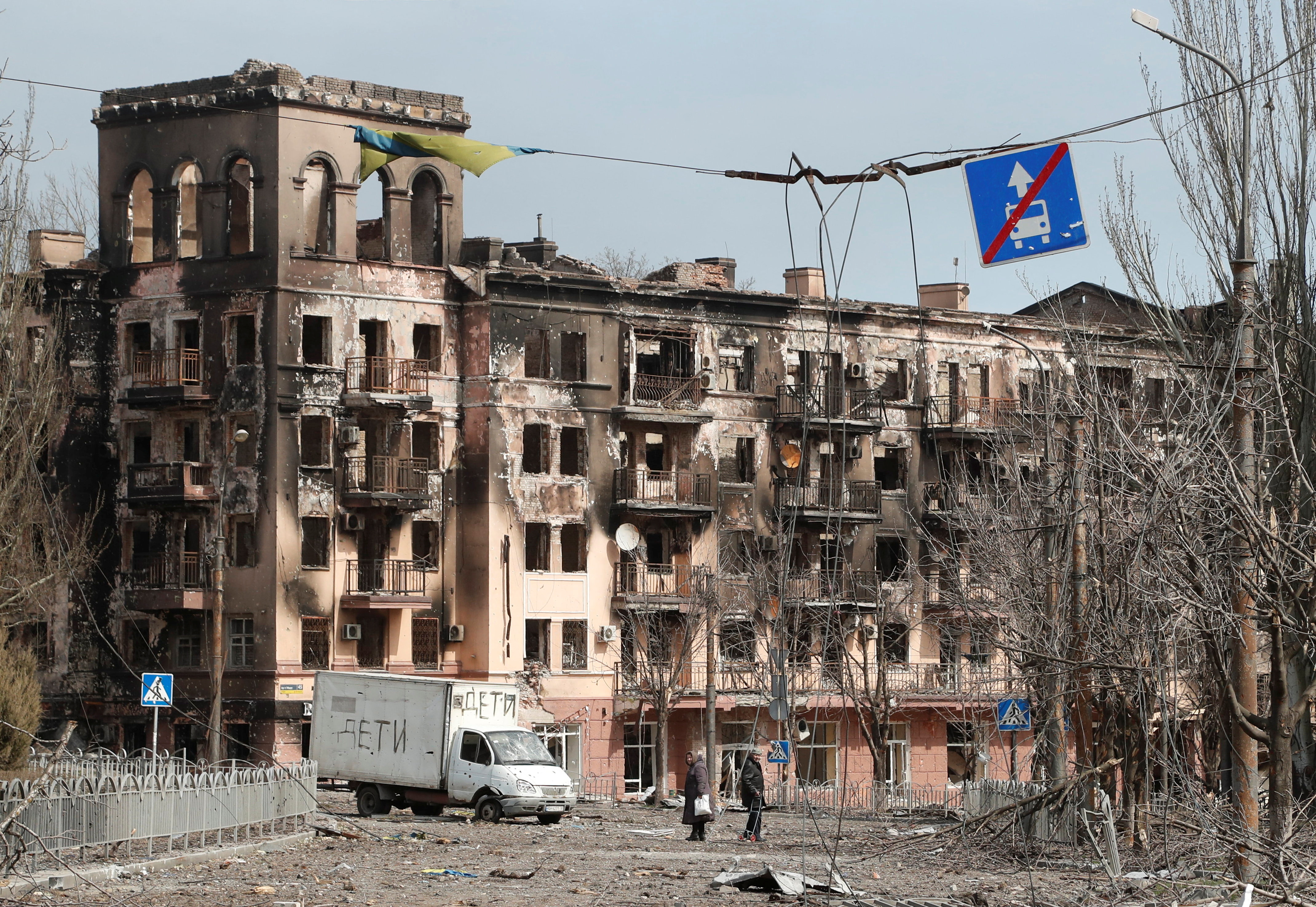 Local residents walk along a street next to a damaged building in Mariupol