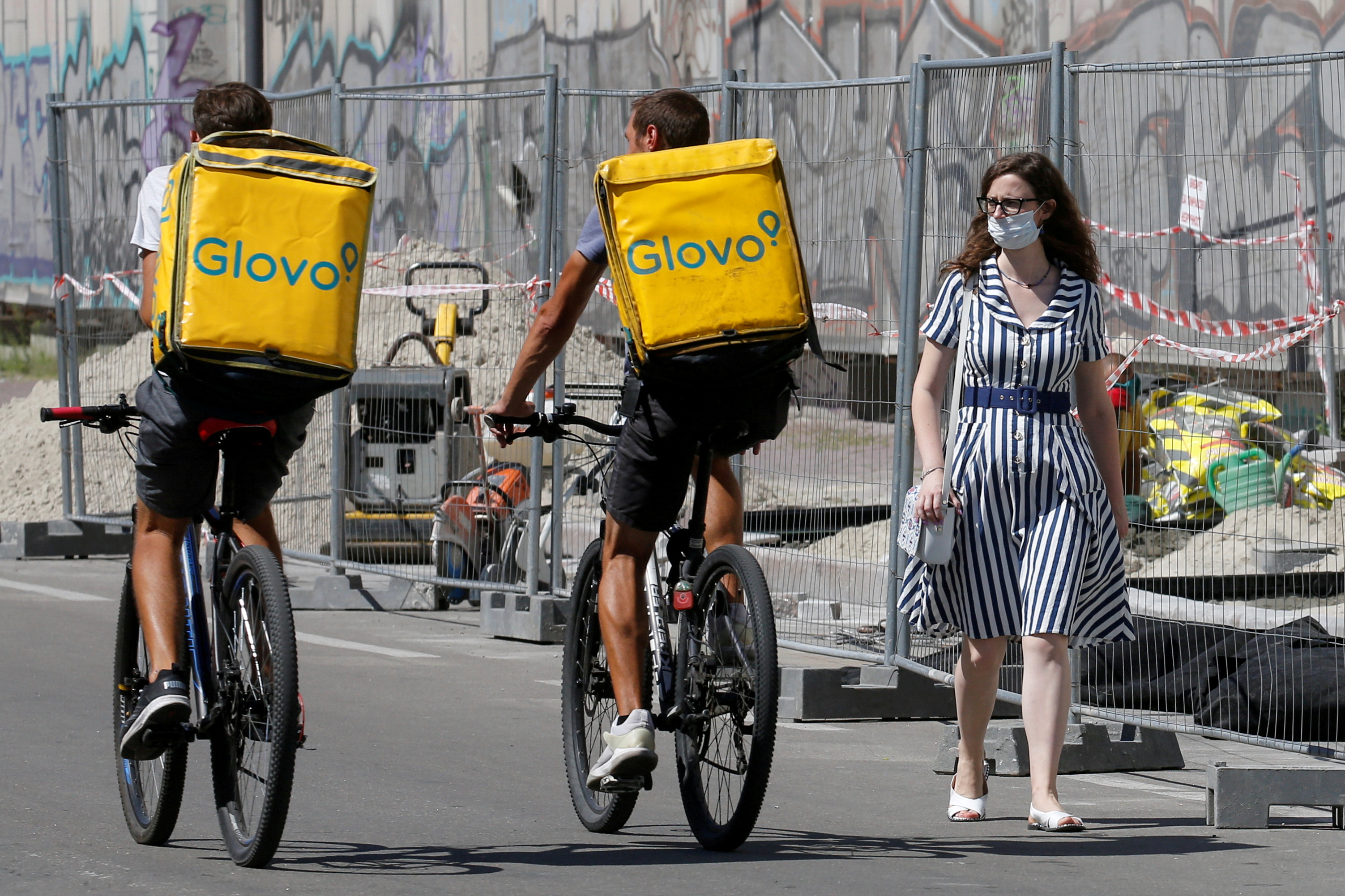 A woman walks past Glovo food delivery couriers in Kyiv