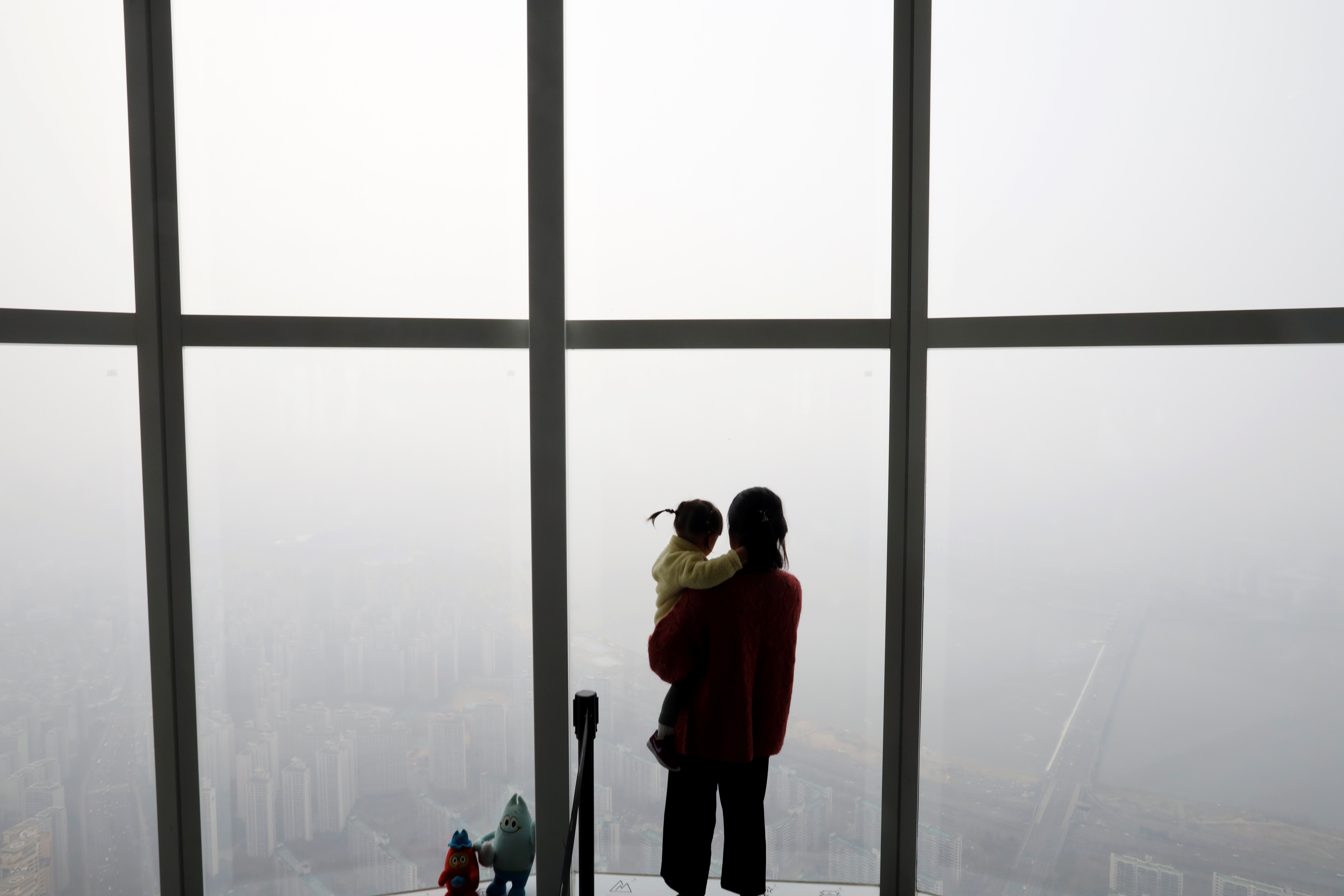 A woman holding her baby in her arms looks at a view of Seoul shrouded by fine dust during a polluted day in Seoul