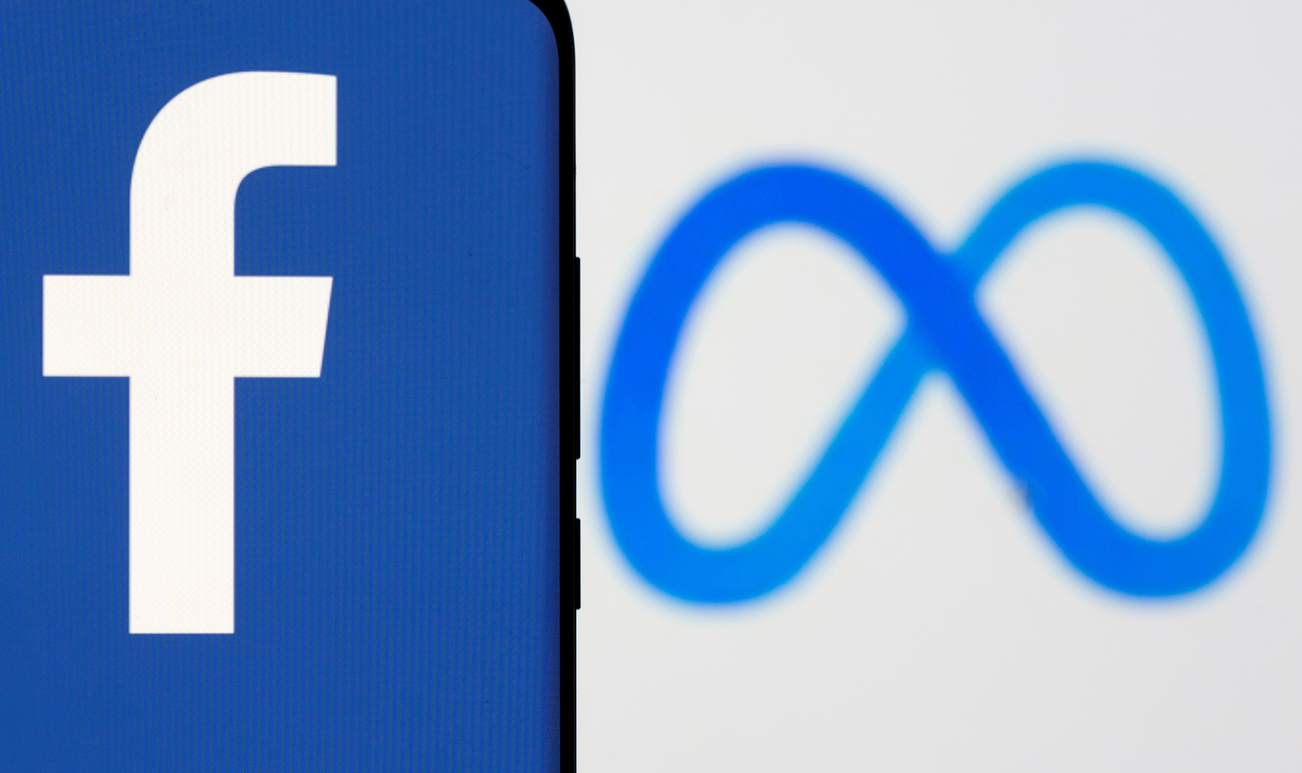 Facebook's new rebrand logo Meta is displayed behind a smartphone with the Facebook logo in this illustration picture